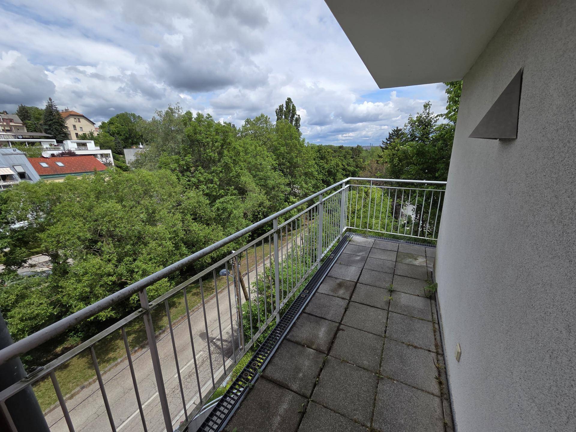 Balkon mit Fliesenboden und Metallgeländer, mit Blick auf die Straße und grüne Umgebung.
