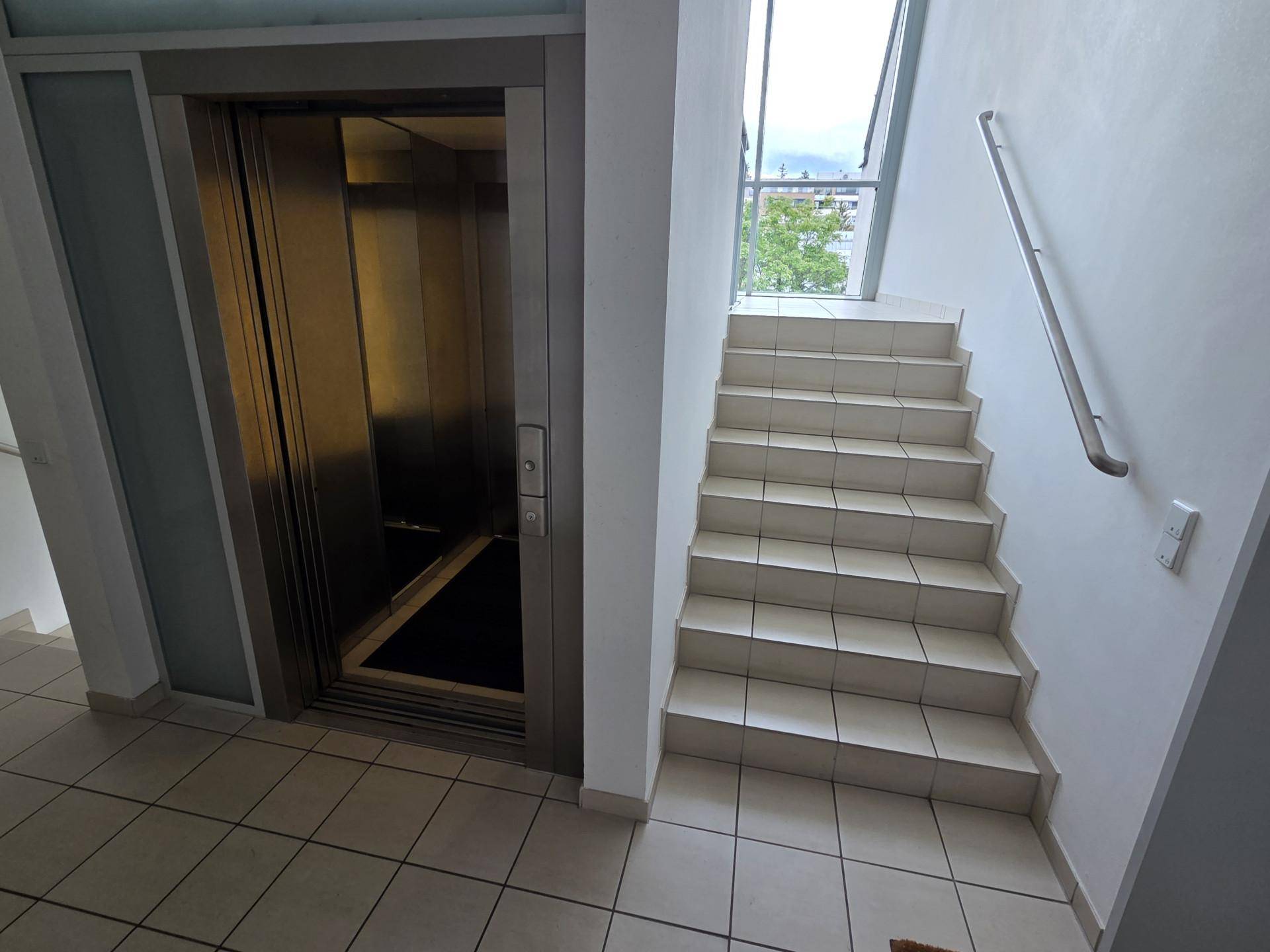 Heller Flur mit Aufzug und Treppe, die zu den oberen Etagen führt.