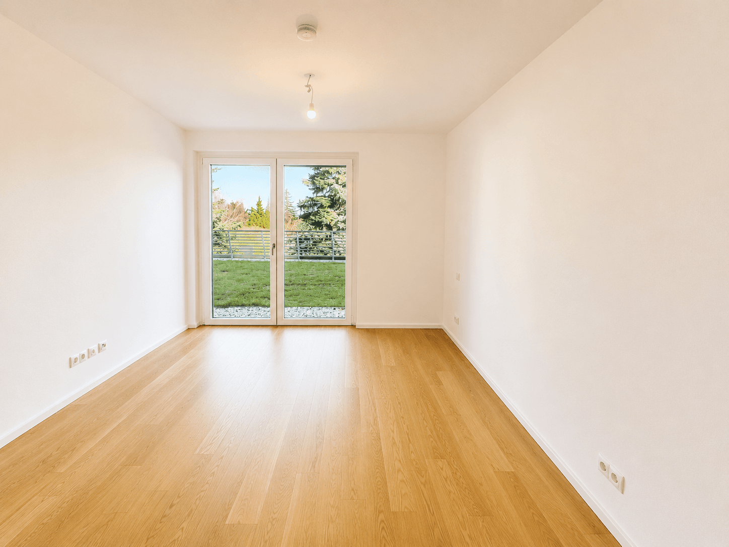 Geräumiges, helles Zimmer mit Holzboden und Balkonzugang, bietet einen grünen Ausblick.