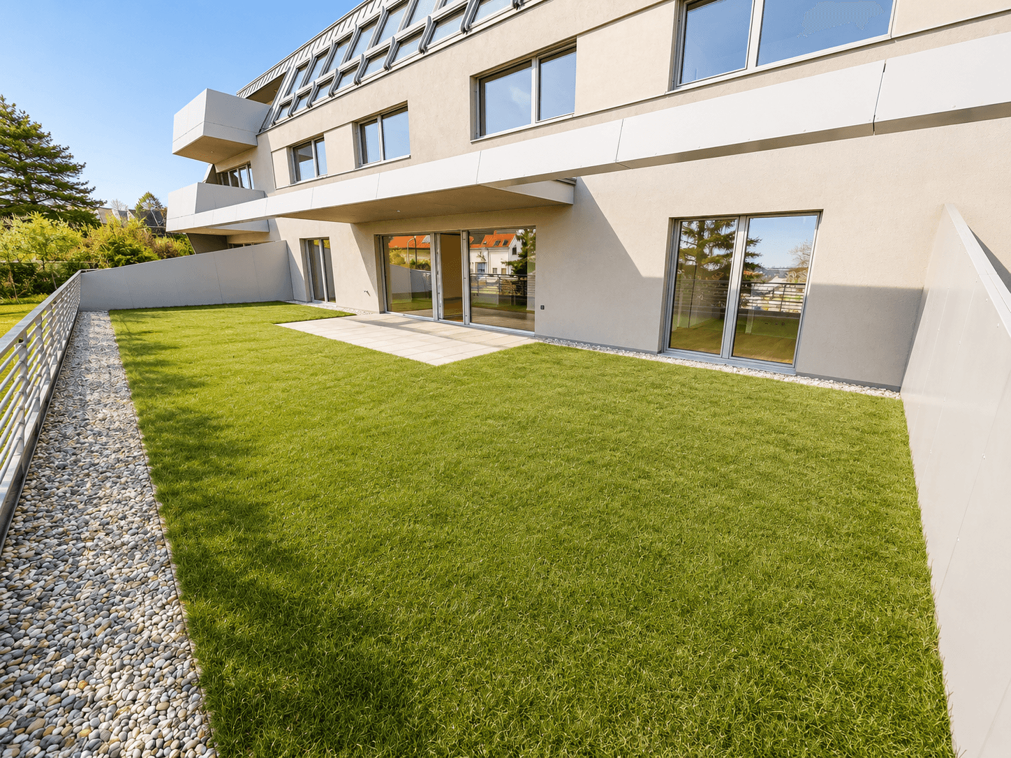 Gepflegter Gartenbereich mit Rasenfläche und Terrasse im Erdgeschoss eines modernen Gebäudes.