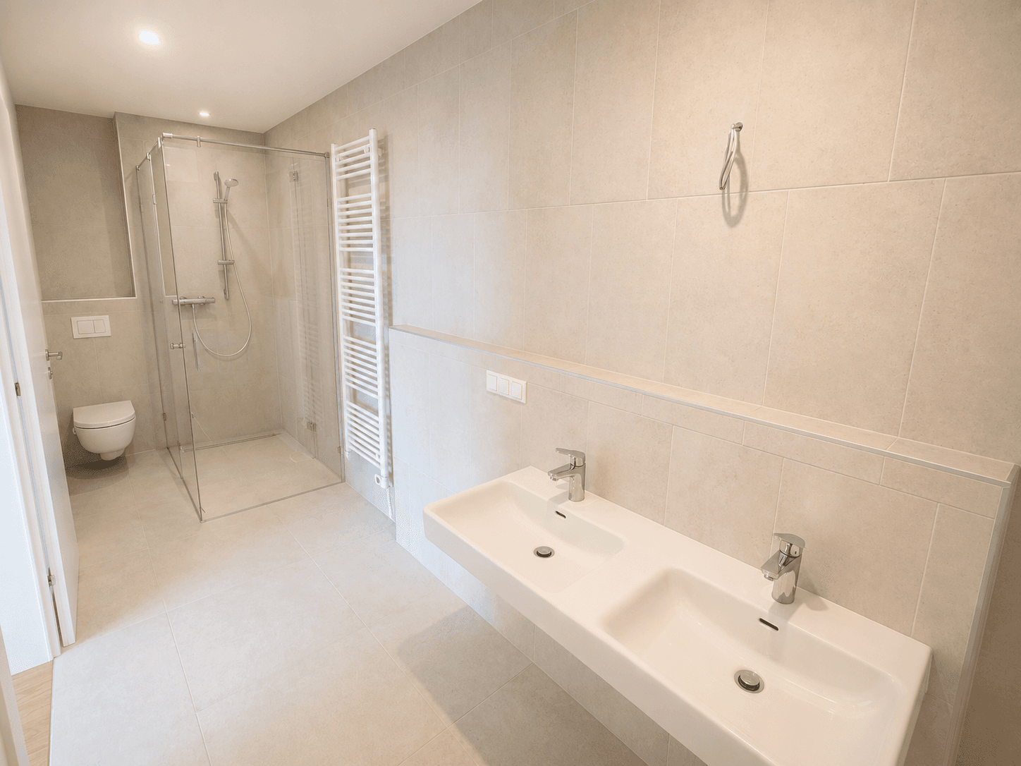 Modernes Badezimmer mit beigefarbenen Fliesen, Doppelwaschbecken, ebenerdiger Dusche und beheiztem Handtuchhalter.