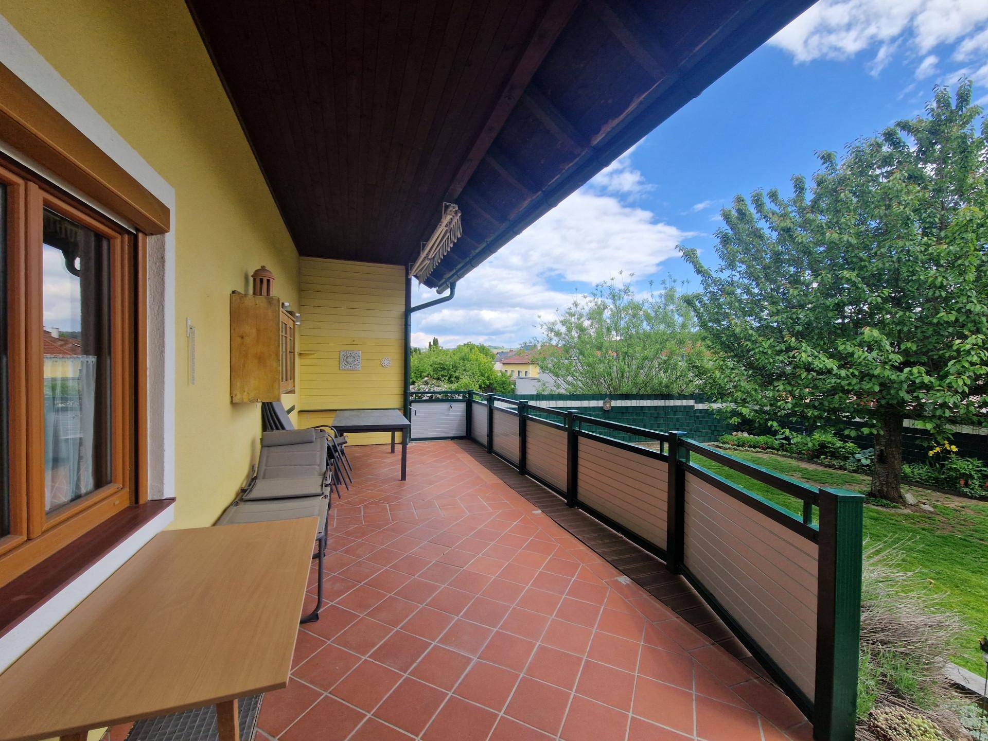 Überdachte Terrasse mit Terrakottafliesen, Sitzgelegenheiten und Blick in den Garten.