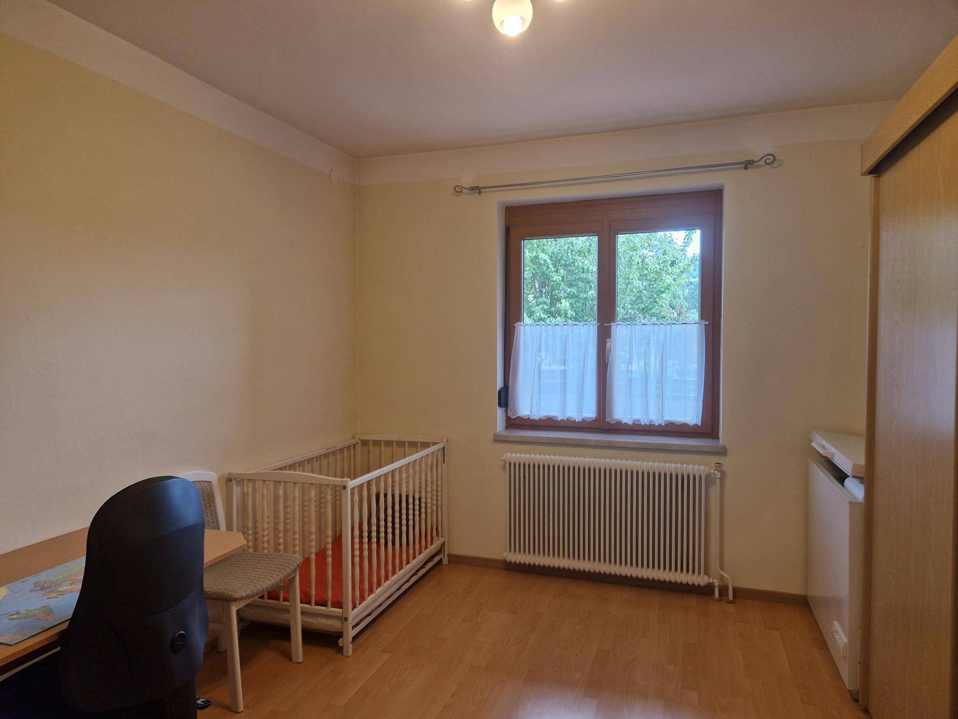 Kinderzimmer oder Gästezimmer mit Gitterbett, Schreibtisch und Fenster.