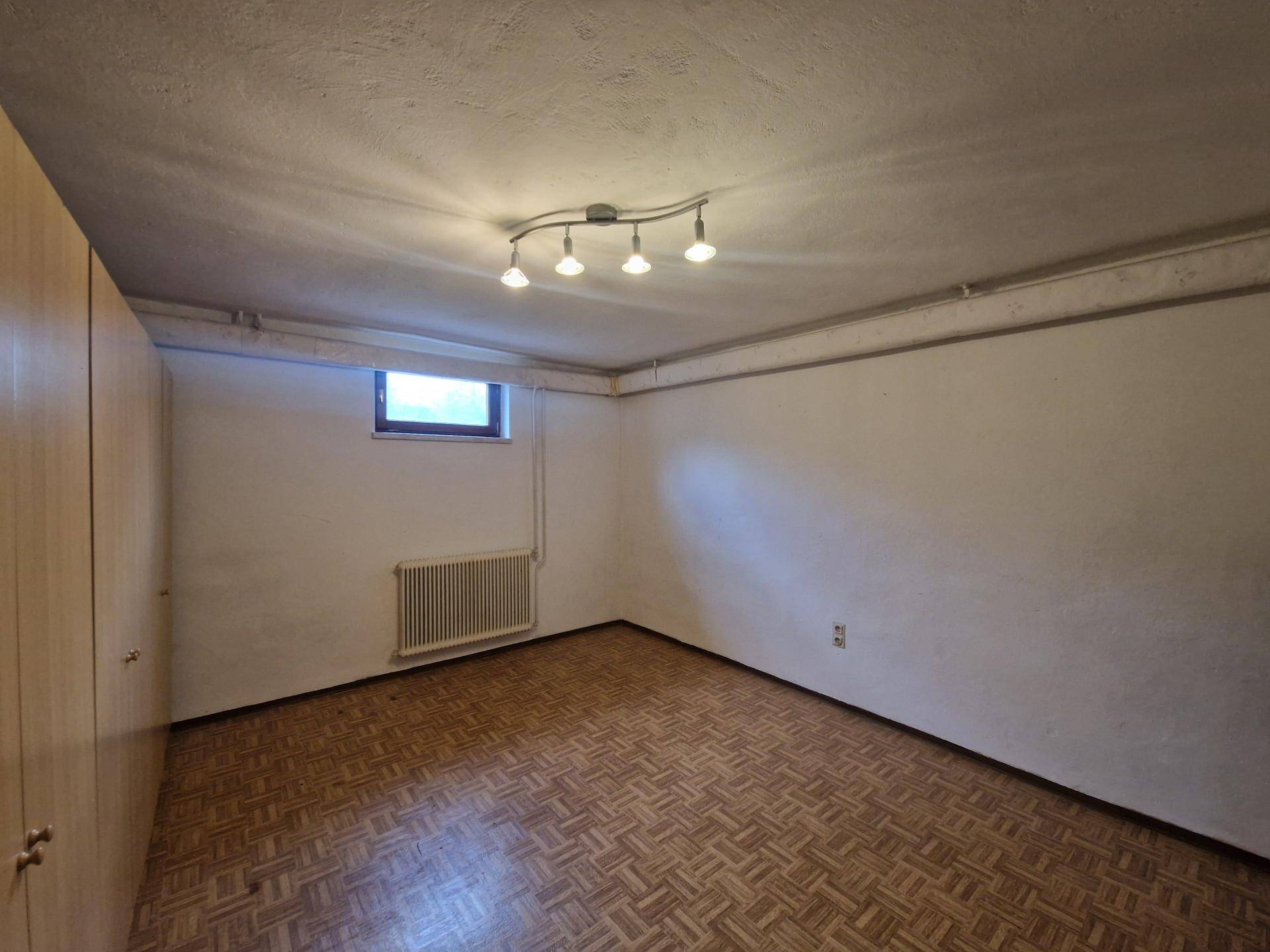 Ausgebauter Kellerraum mit Parkettboden, Einbauschränken und Fenster.