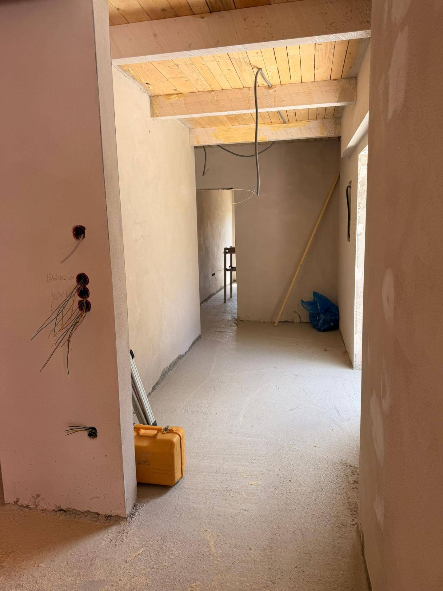 Unfertiger Flur mit Holzbalkendecke, Betonboden und sichtbaren Elektroinstallationen.