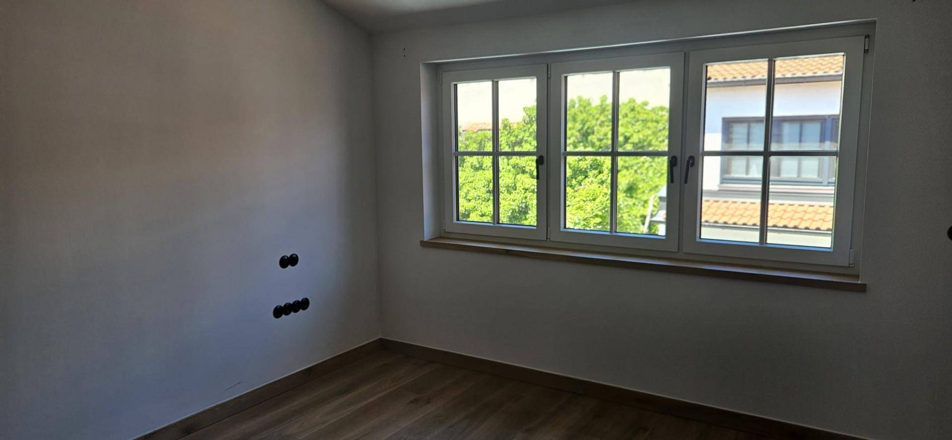 Leerer Raum mit Holzboden und großem Fenster, bereit für die Einrichtung.