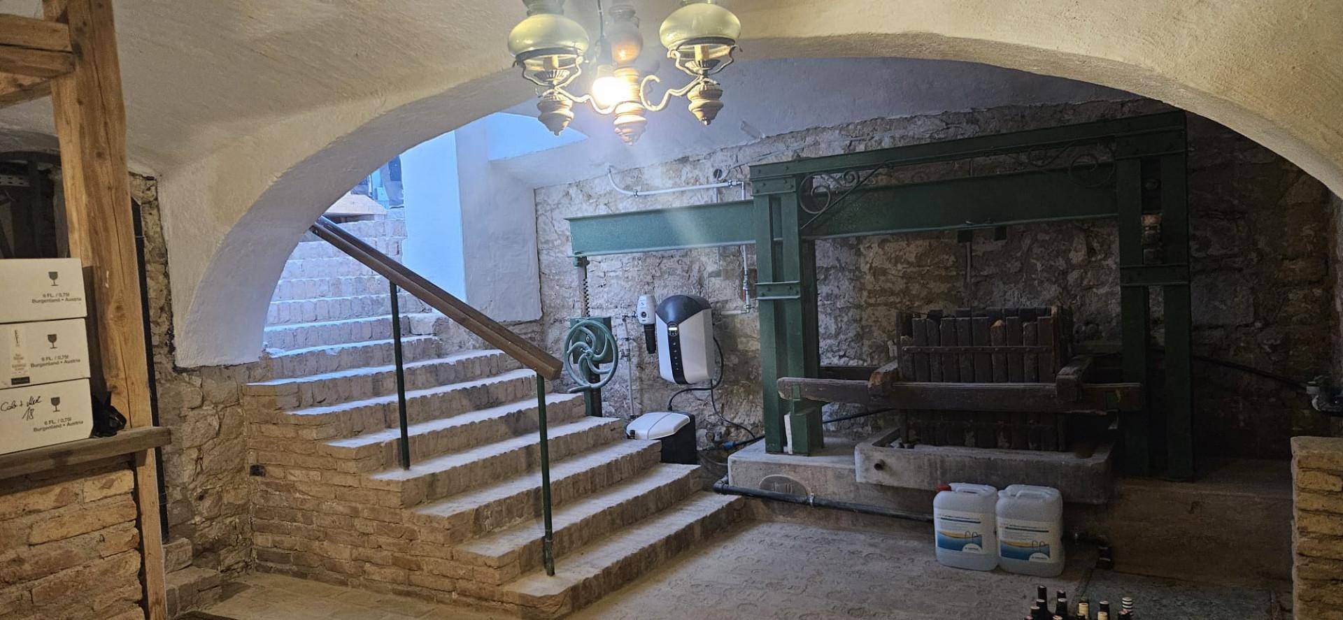 Rustikaler Keller mit alter Weinpresse, Steintreppe und traditioneller Beleuchtung.