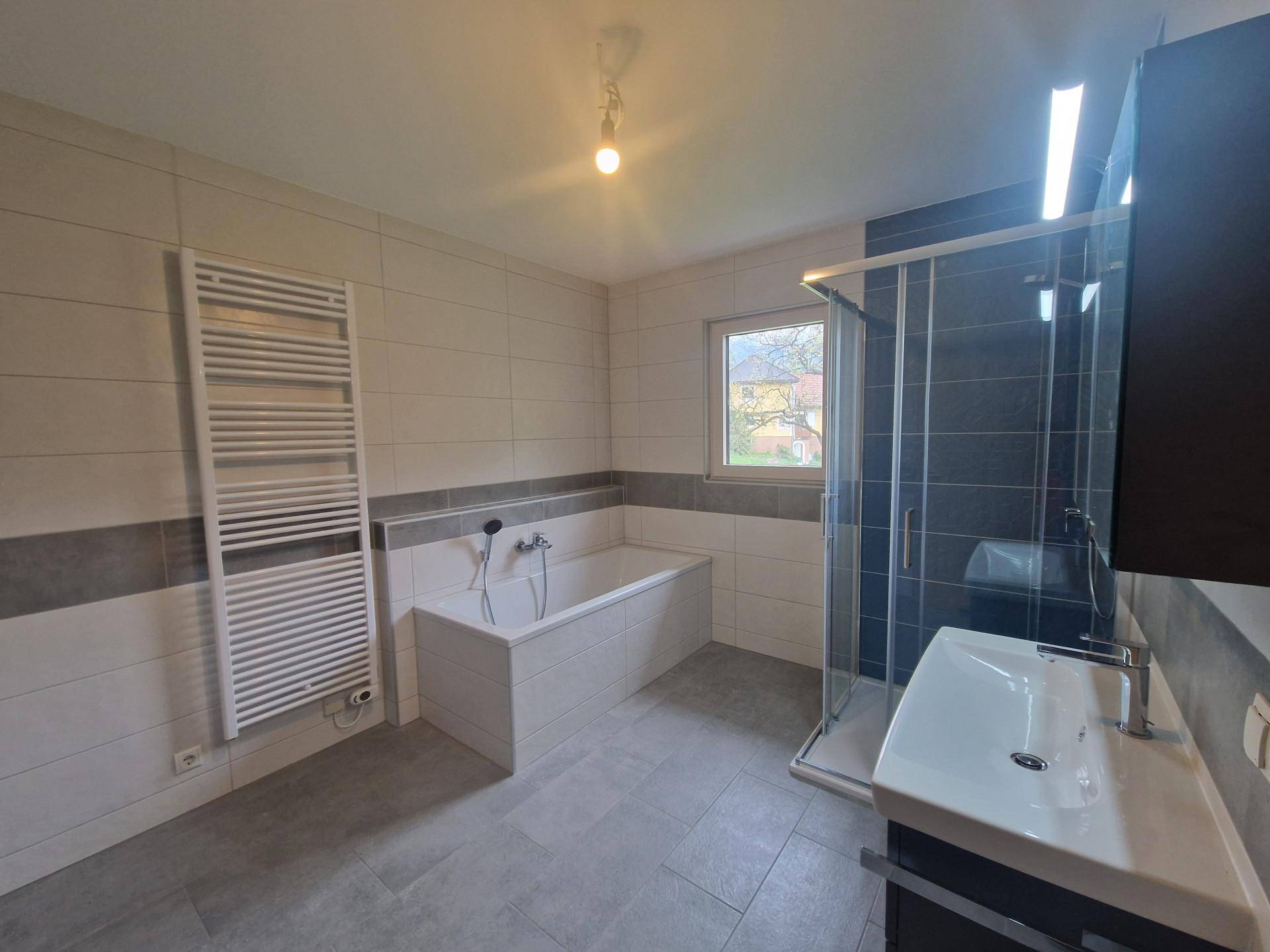 Modernes Badezimmer mit Badewanne, Dusche, beheiztem Handtuchhalter und Fenster.