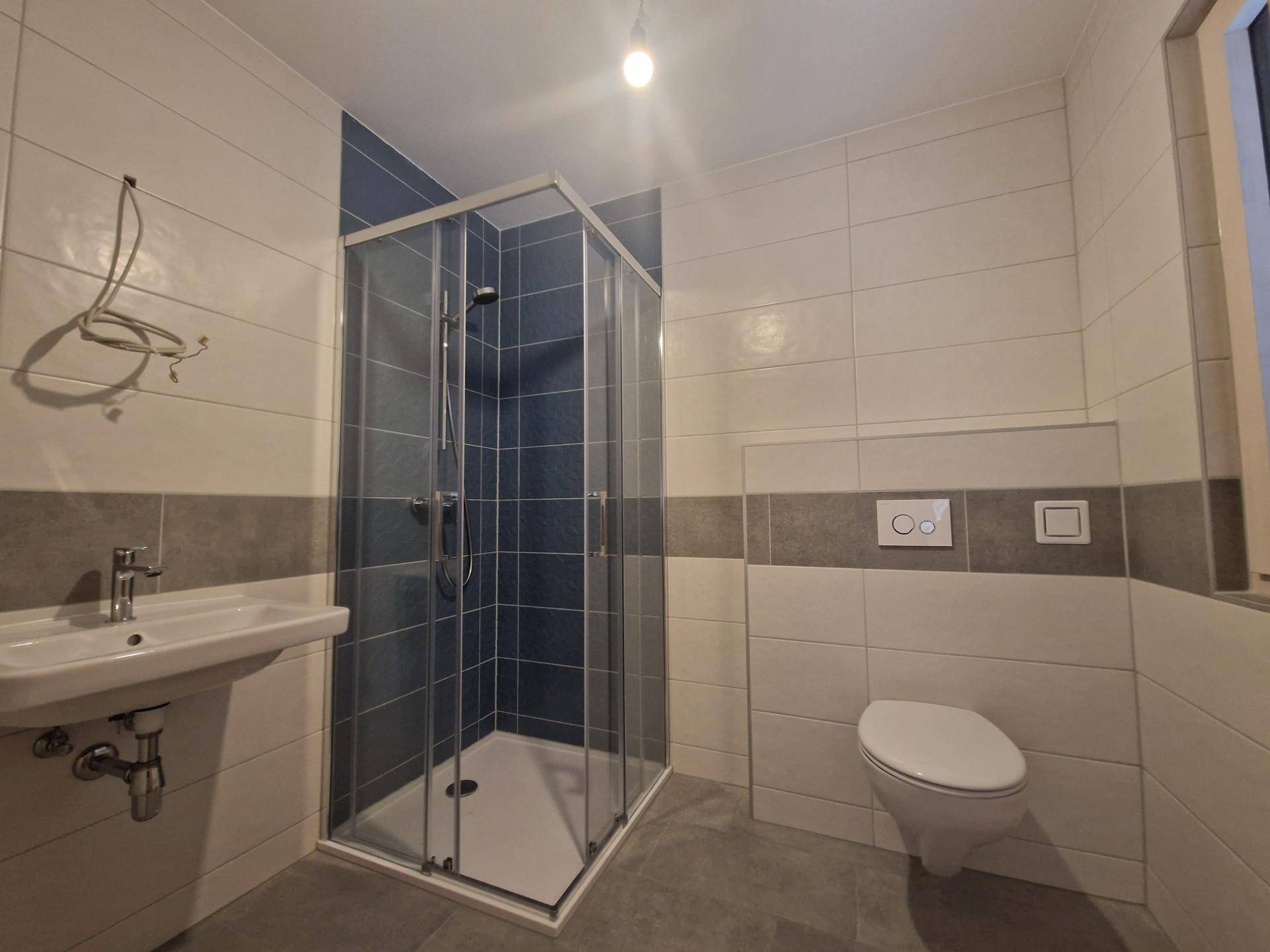 Zeitgemäßes Badezimmer mit Duschkabine, Wand-WC und Waschbecken in neutralen Farben.
