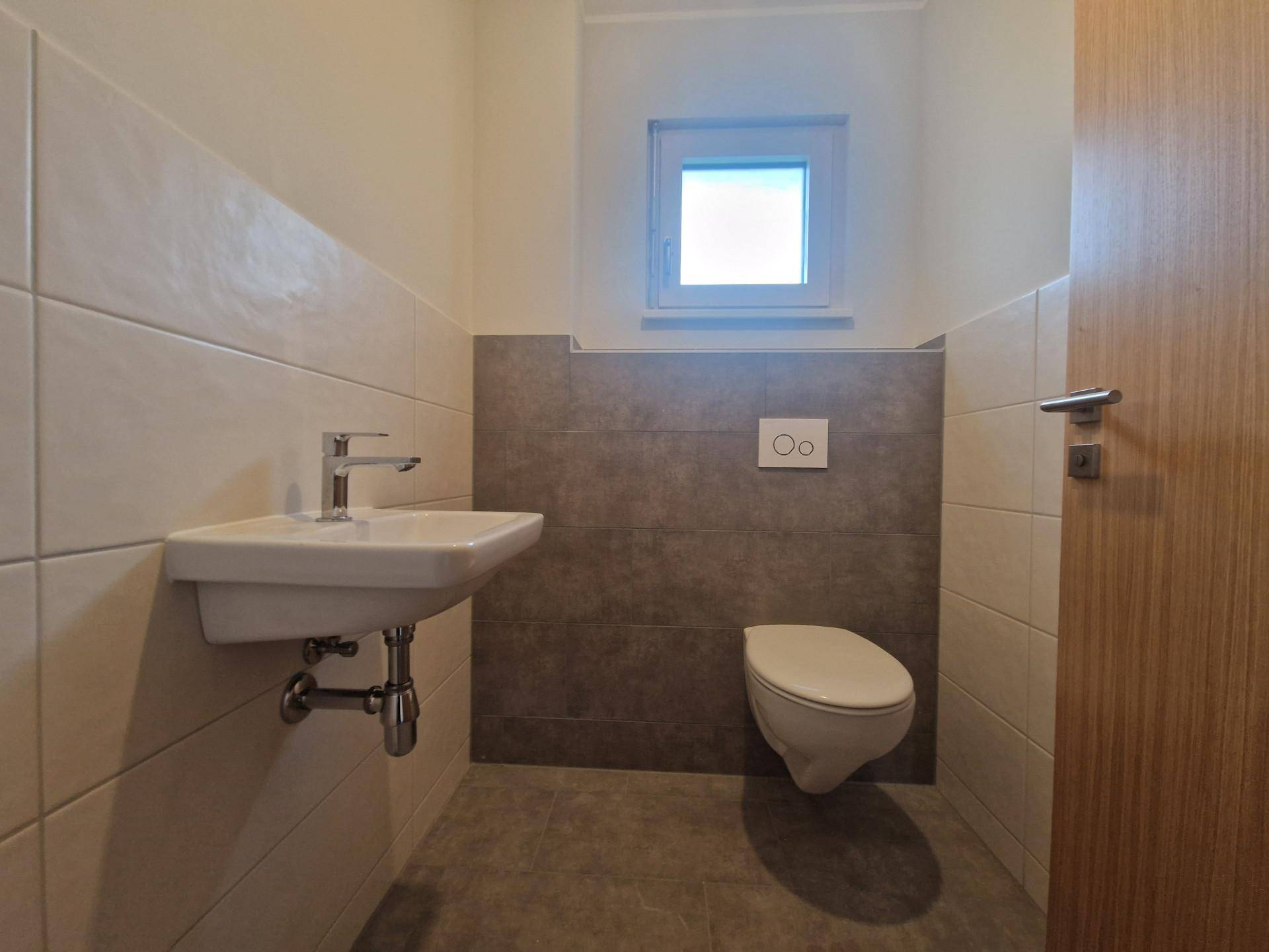 Praktisches Gäste-WC mit Wand-WC, kleinem Waschbecken und Fenster für Tageslicht.