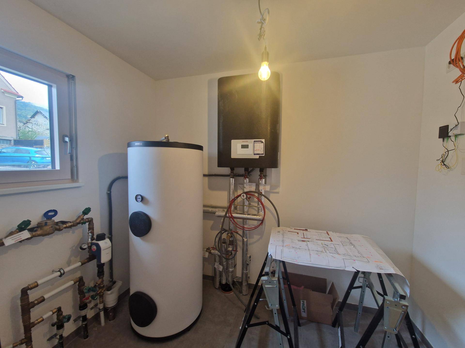 Technikraum mit Warmwasserspeicher und Heizungsanlage, gut beleuchtet durch ein Fenster.