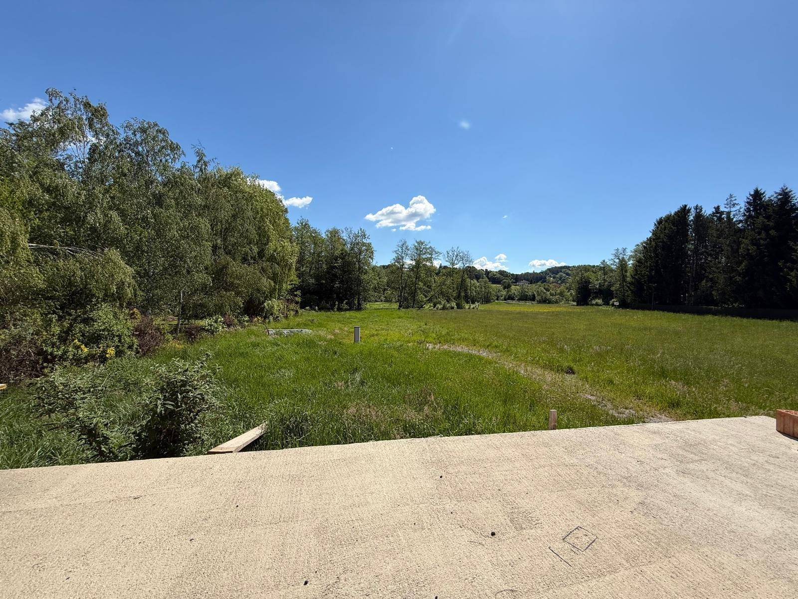 Weitläufiger Blick über grüne Wiesen und Wälder unter einem klaren blauen Himmel von einer unfertigen Terrasse.