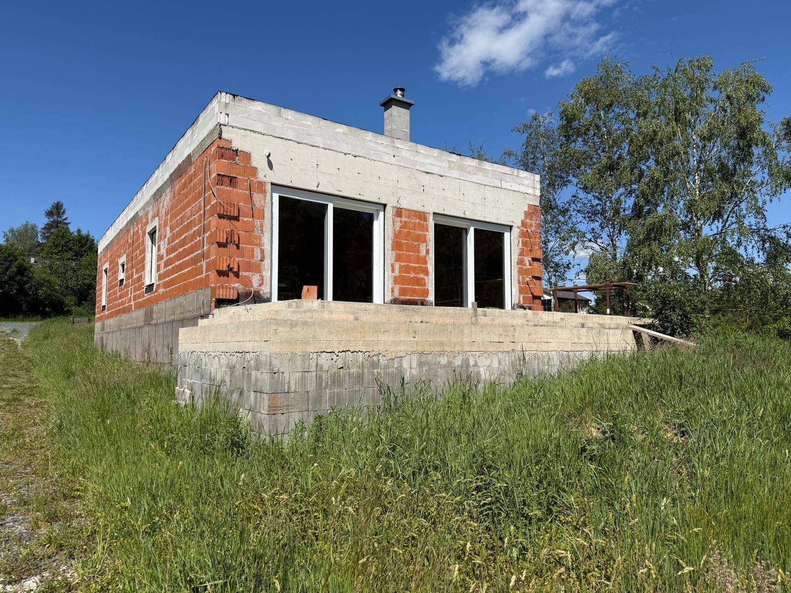Rohbau eines modernen Hauses mit großen Fensteröffnungen und Ziegelwänden, bereit für den weiteren Ausbau.