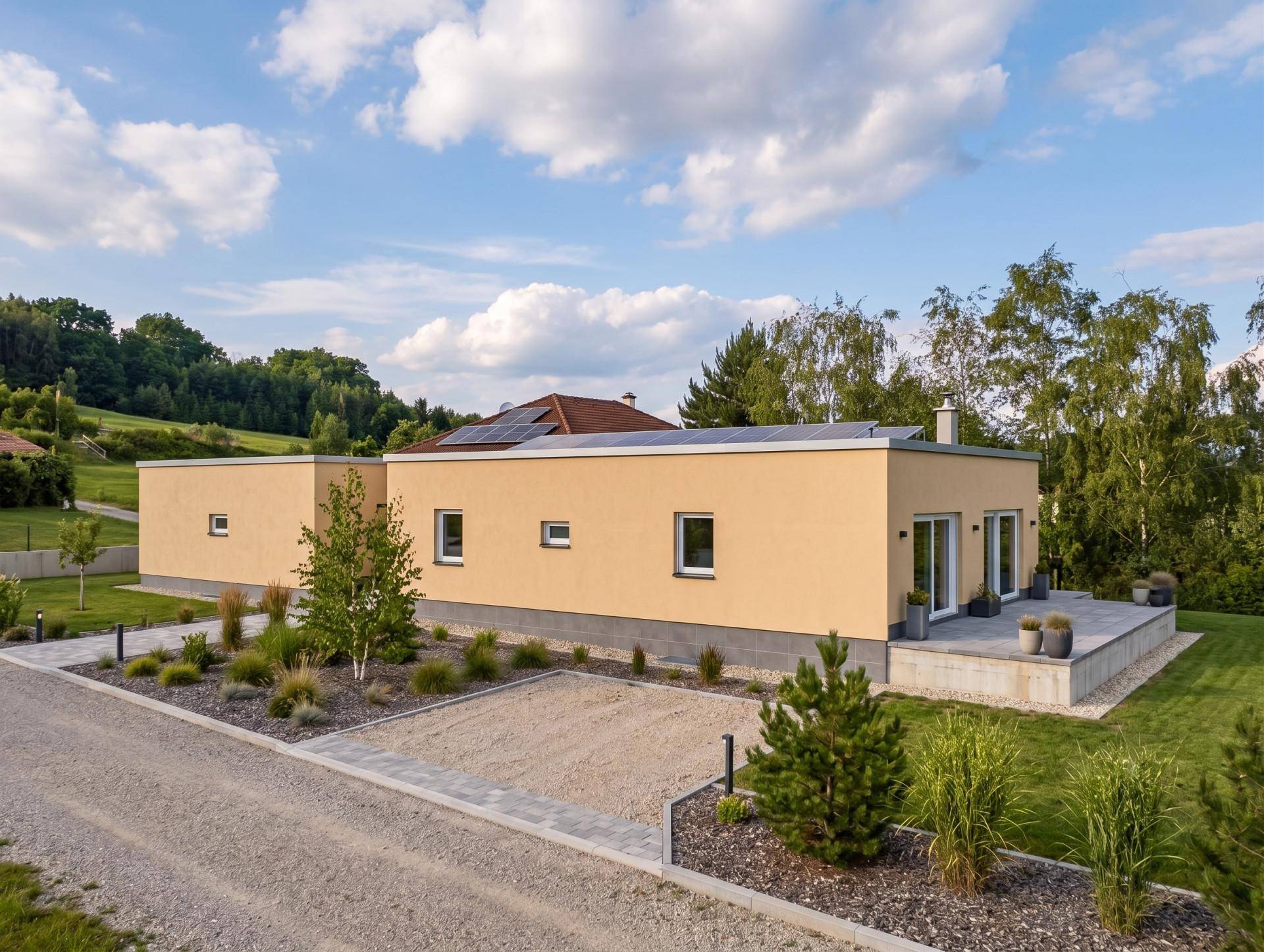 Modernes Einfamilienhaus mit gelber Fassade, Flachdach mit Solaranlage und gepflegter Außenanlage aus der Vogelperspektive.