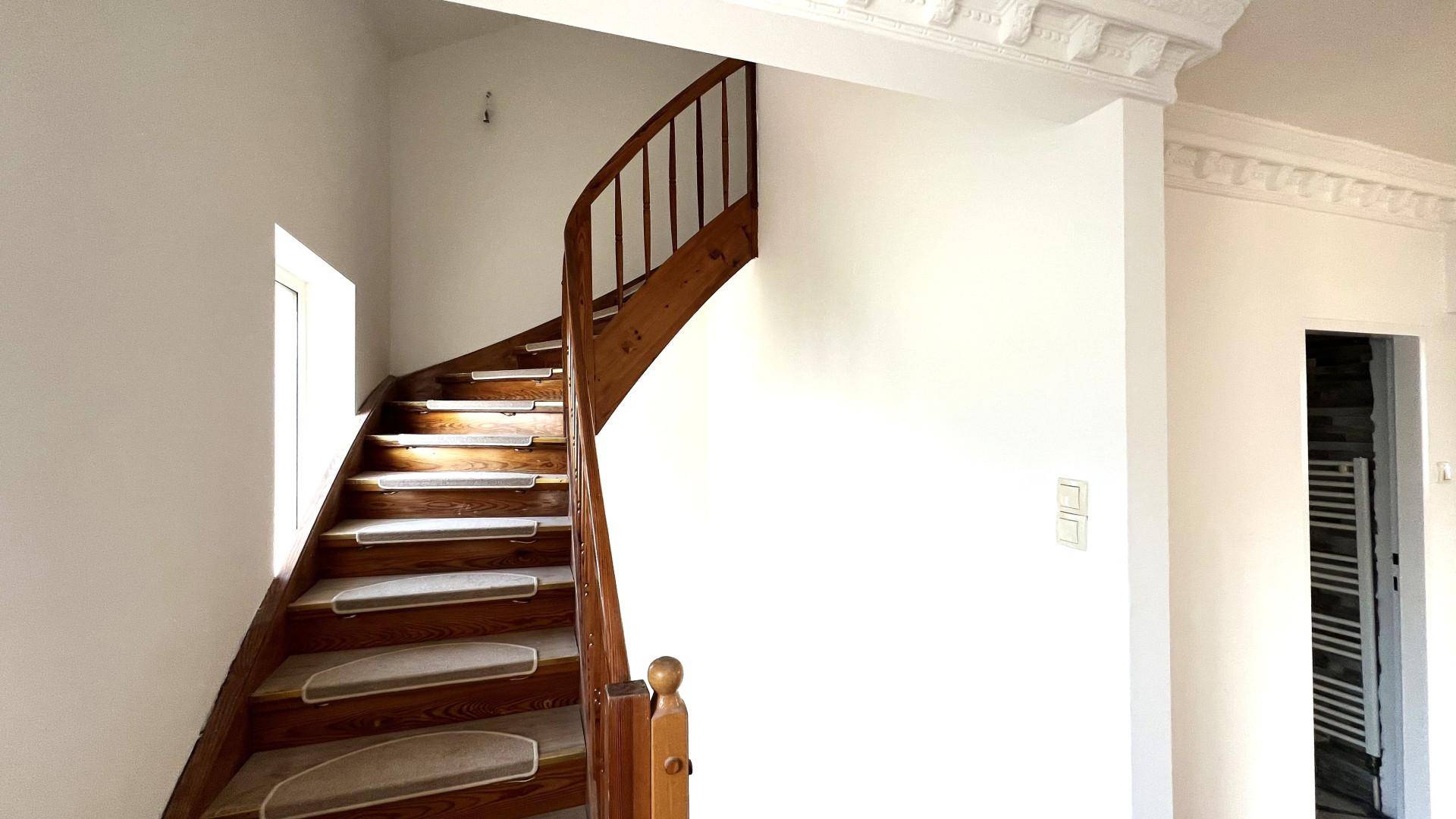 Elegantes Treppenhaus mit einer Holzwendeltreppe und dekorativer Stuckverzierung an der Decke.