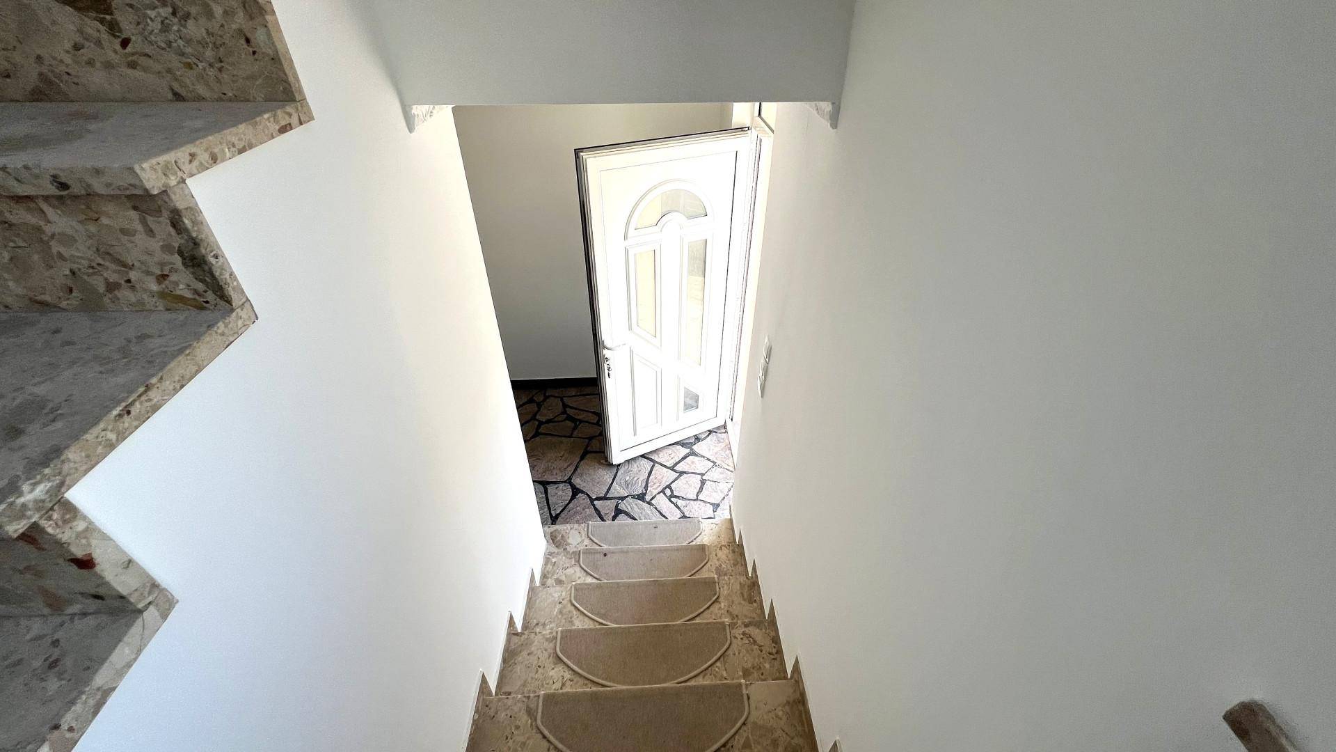 Treppenhaus mit Steinstufen und einer weißen Eingangstür, die ins Freie führt.