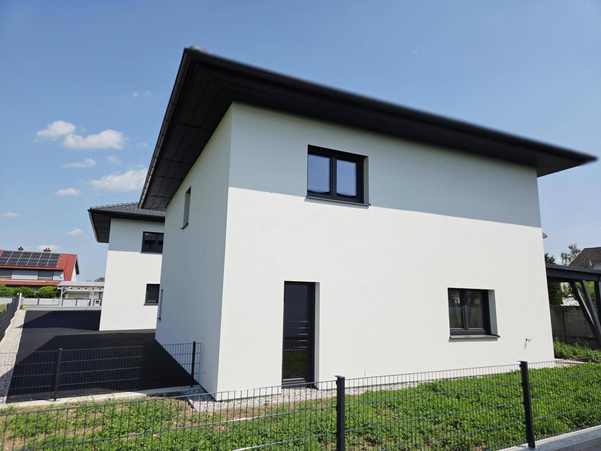 Seitenansicht eines modernen Einfamilienhauses mit dunklen Fenstern und Dach unter strahlendem Himmel.