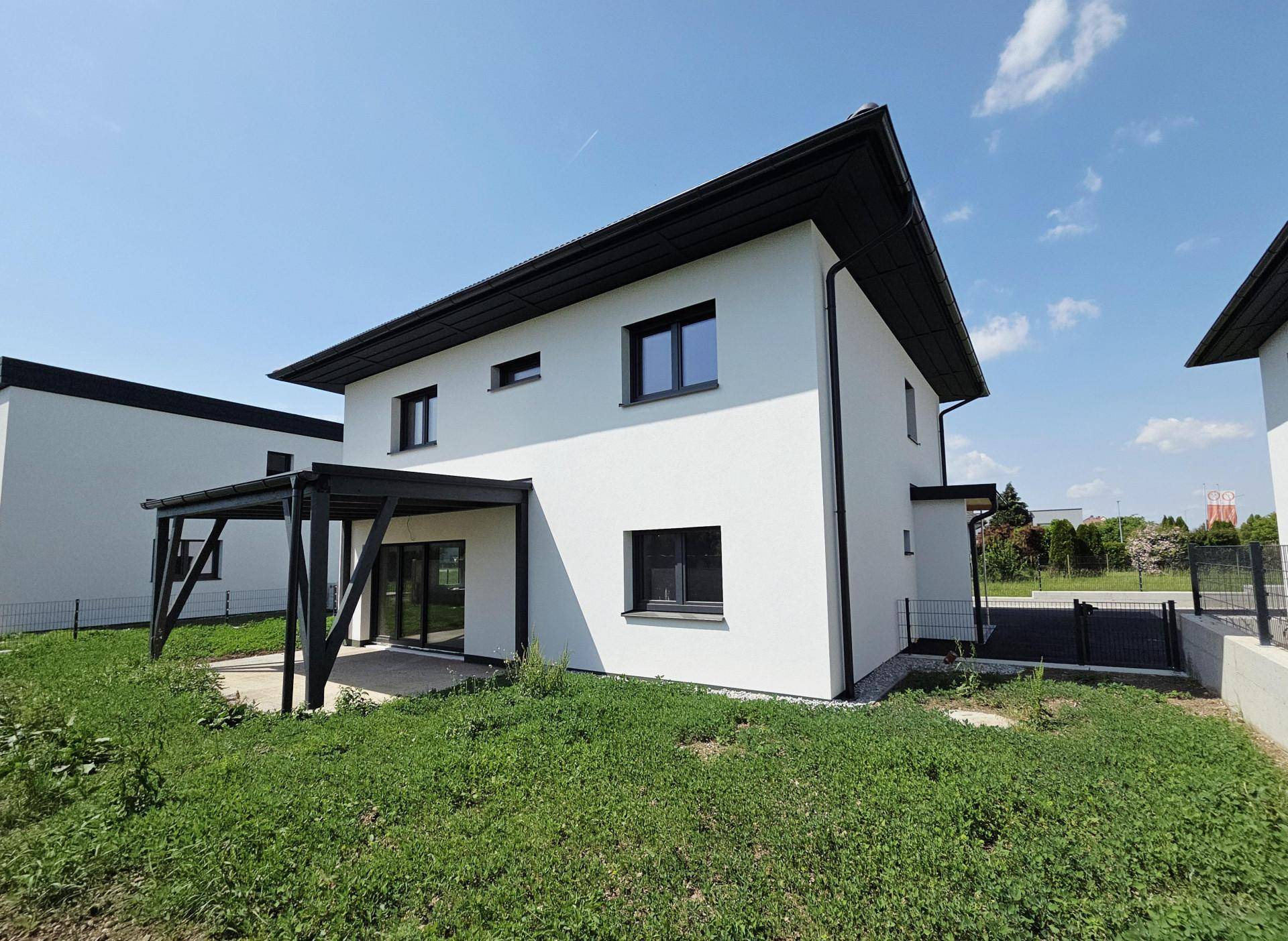 Modernes Einfamilienhaus mit überdachter Terrasse und Gartenbereich unter blauem Himmel.