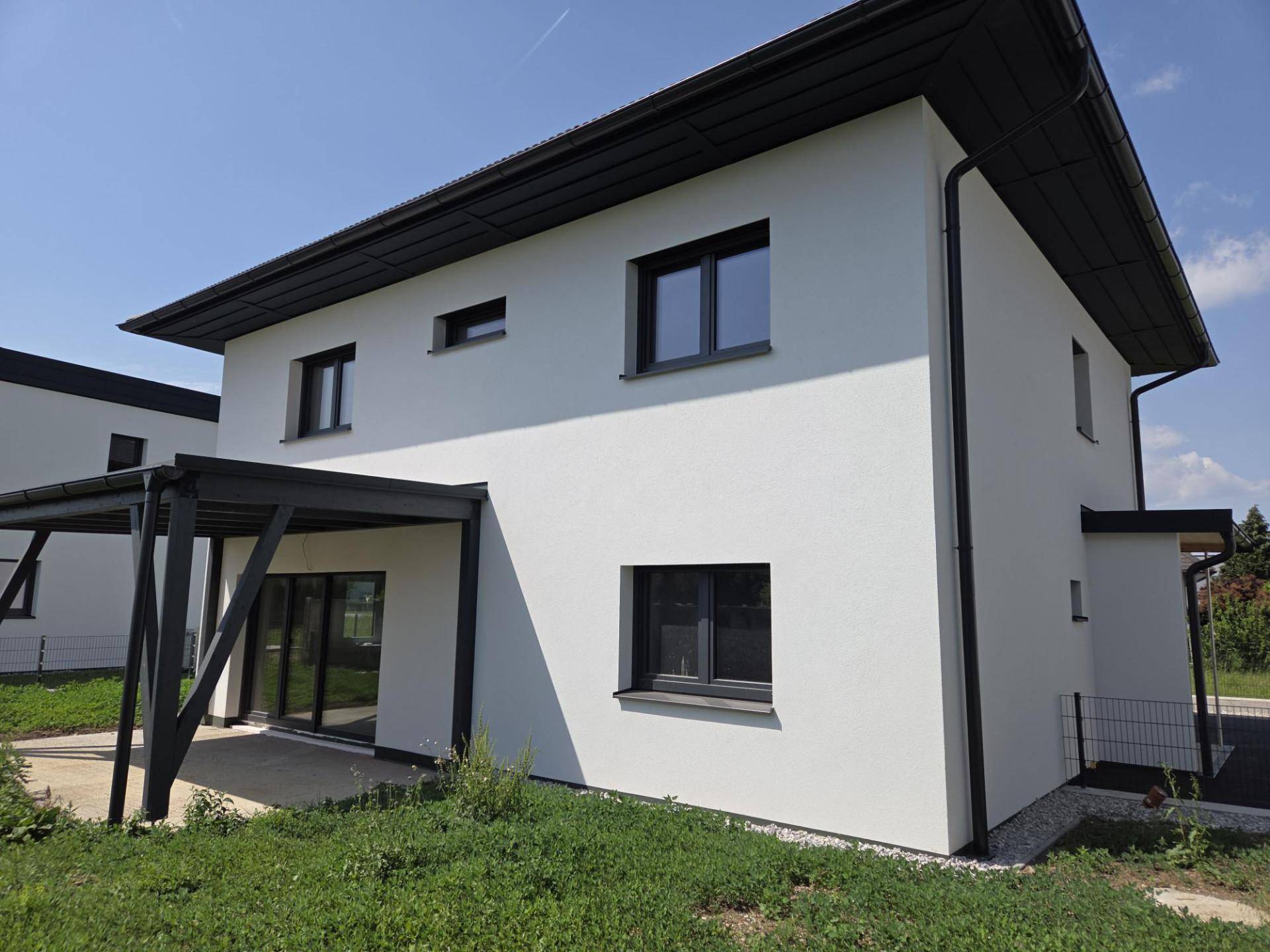 Modernes Einfamilienhaus mit überdachter Terrasse und angrenzendem Rasenbereich unter blauem Himmel.