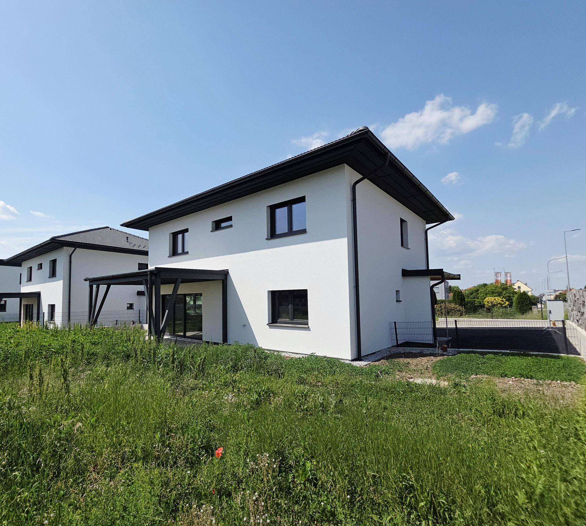 Neubau-Einfamilienhaus mit überdachter Terrasse und weitem Blick ins Grüne an einem sonnigen Tag.