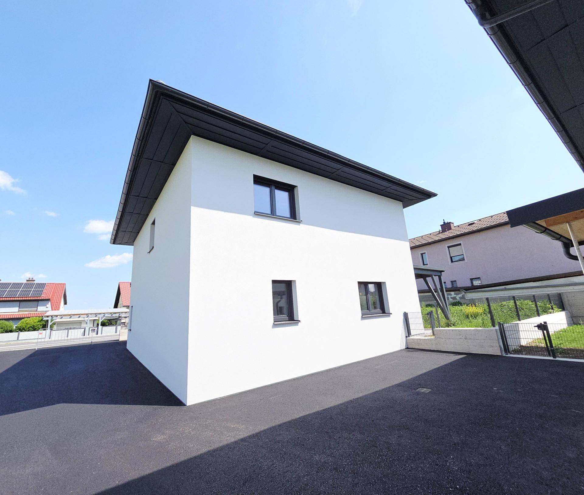 Seitenansicht eines modernen Einfamilienhauses mit asphaltierter Zufahrt und angrenzendem Garten.