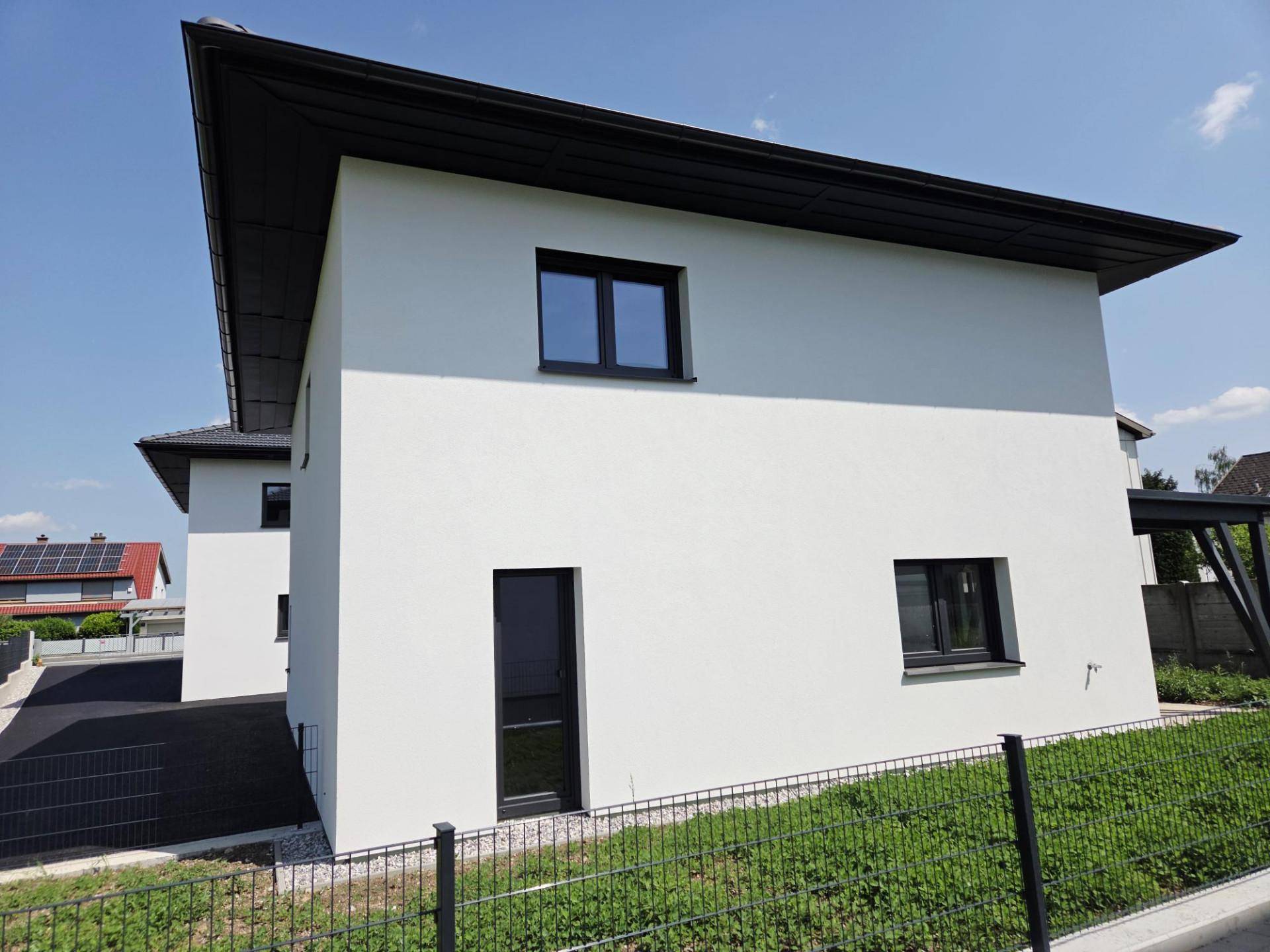 Seitenansicht eines modernen Einfamilienhauses mit dunklen Fenstern und klarem Design.