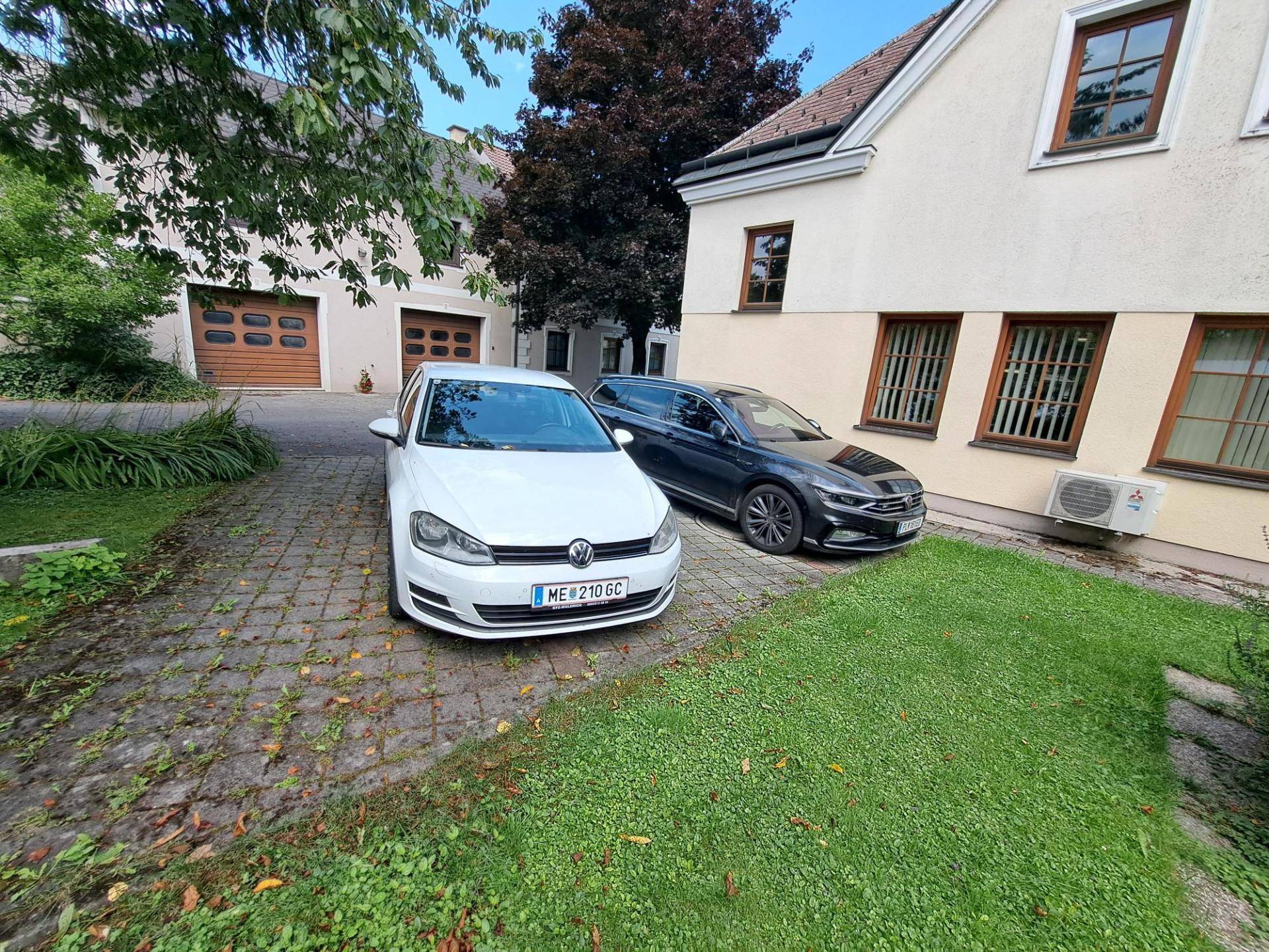 Einfahrt mit zwei geparkten Autos und einem kleinen Rasenbereich neben dem Gebäude.