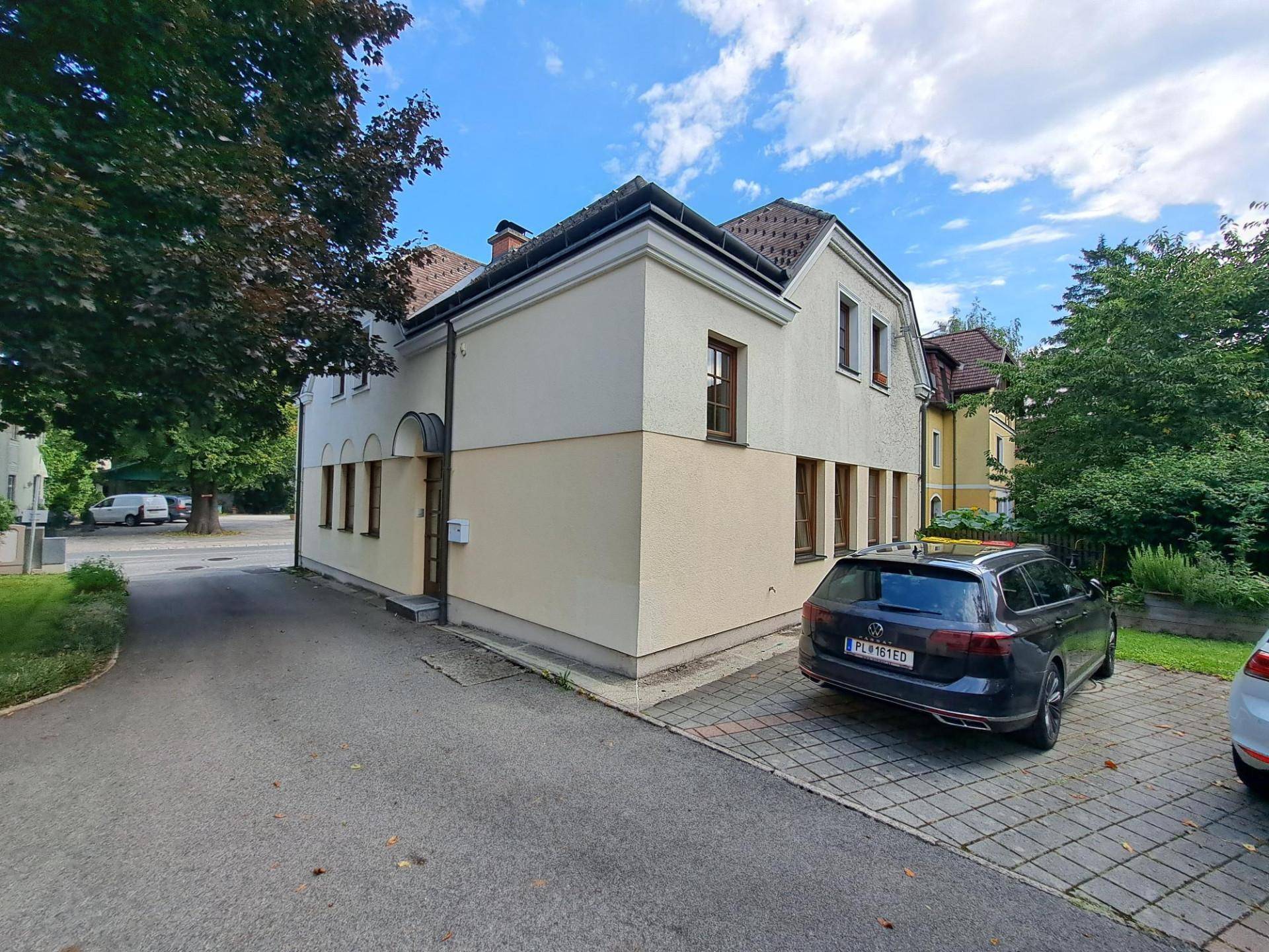 Seitenansicht des Gebäudes mit Zufahrt und geparktem Fahrzeug auf dem Grundstück.