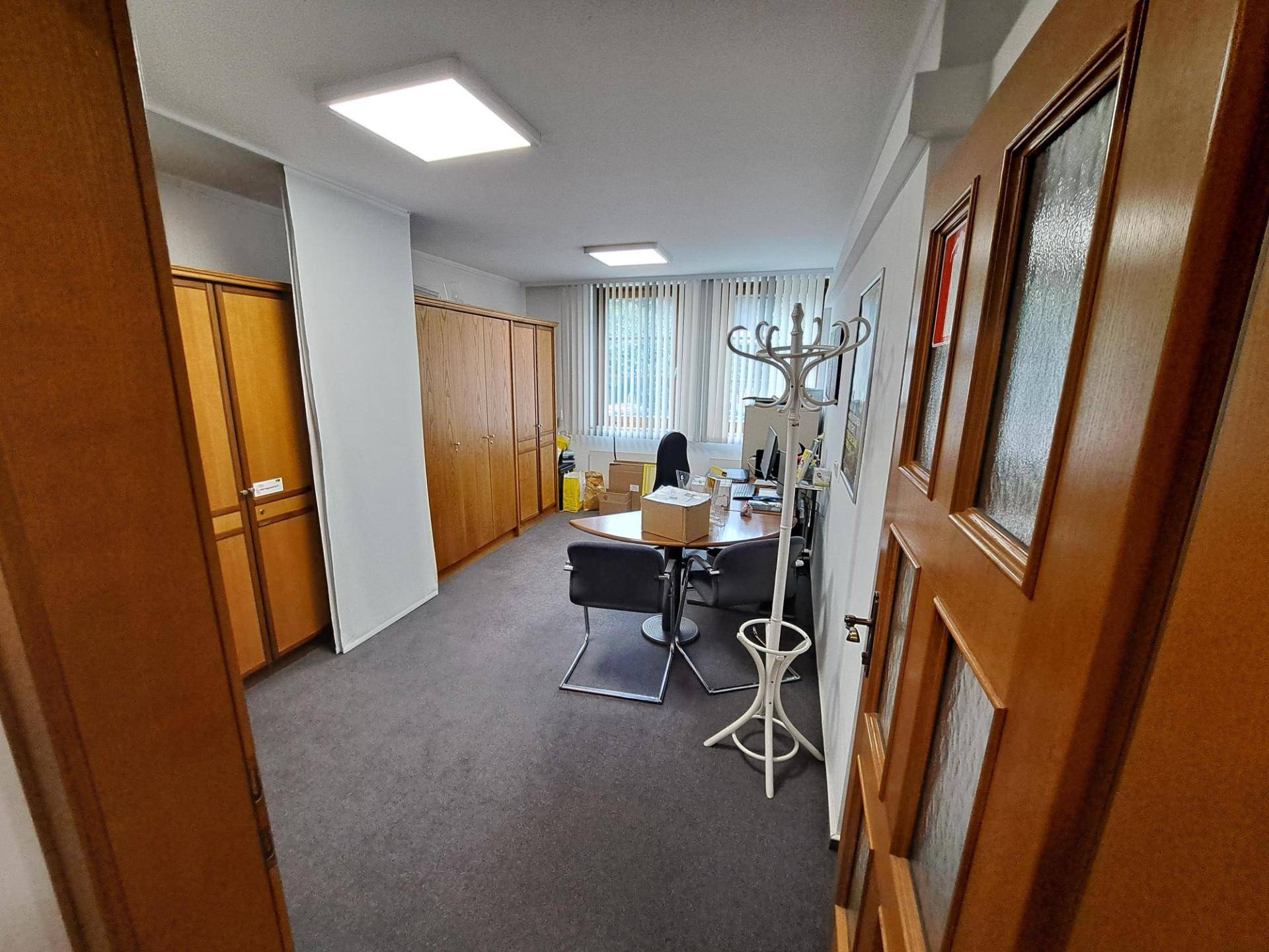 Geräumiges Büro mit Teppichboden, Holzschränken und großem Fenster für natürliches Licht.
