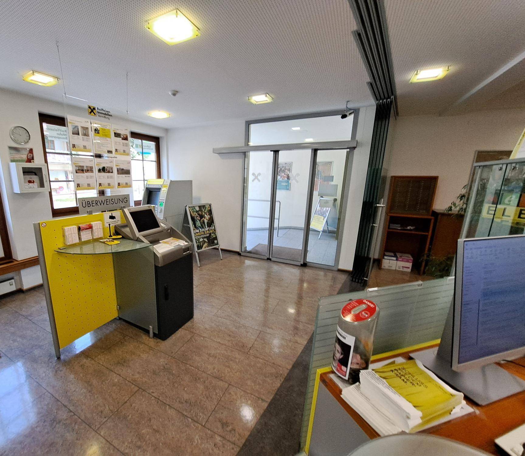 Kundenbereich einer Bank mit Selbstbedienungsterminals, Fliesenboden und natürlichem Lichteinfall.