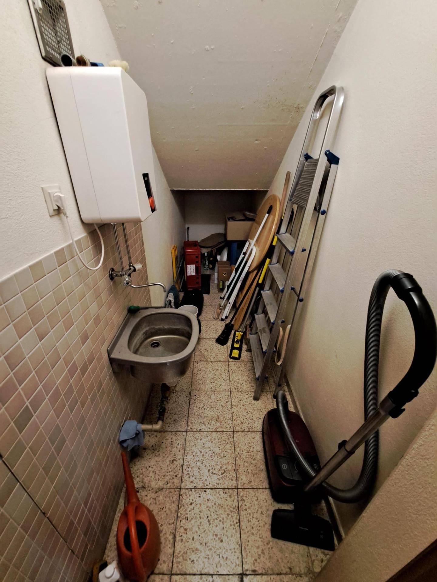 Abstellraum im Keller mit Waschbecken, Boiler und Reinigungsgeräten für den täglichen Gebrauch.