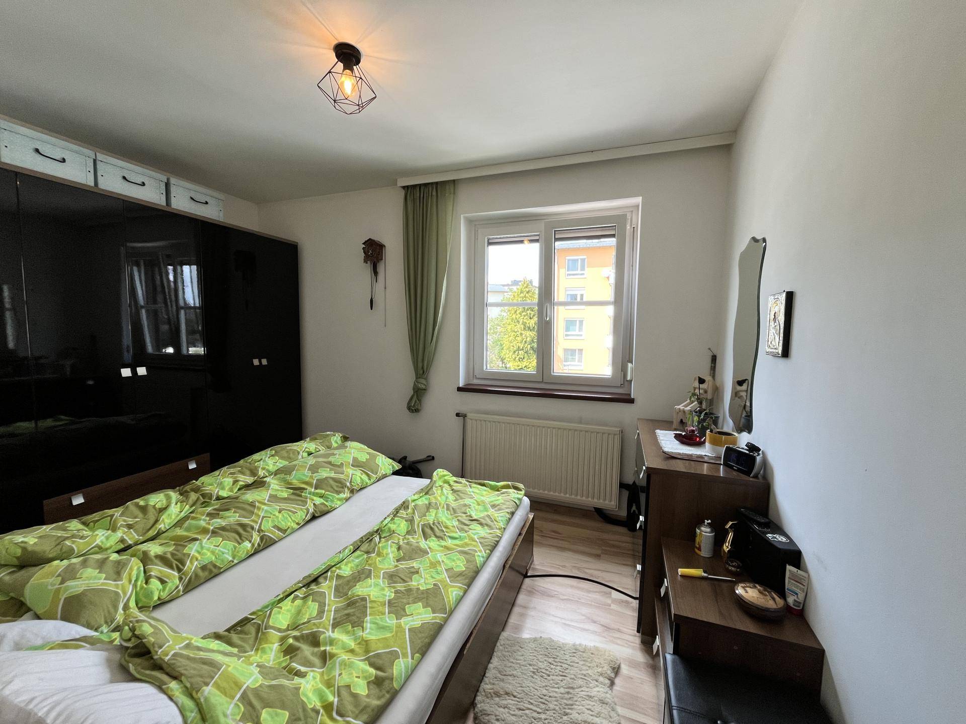 Schlafzimmer mit großem Bett, dunklem Kleiderschrank und Fenster für natürliches Licht am Tag.