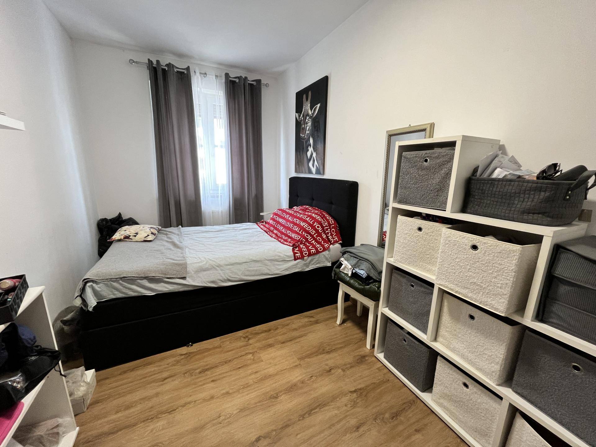 Gemütliches Schlafzimmer mit Einzelbett, praktischen Regalen und Fenster mit grauen Vorhängen.