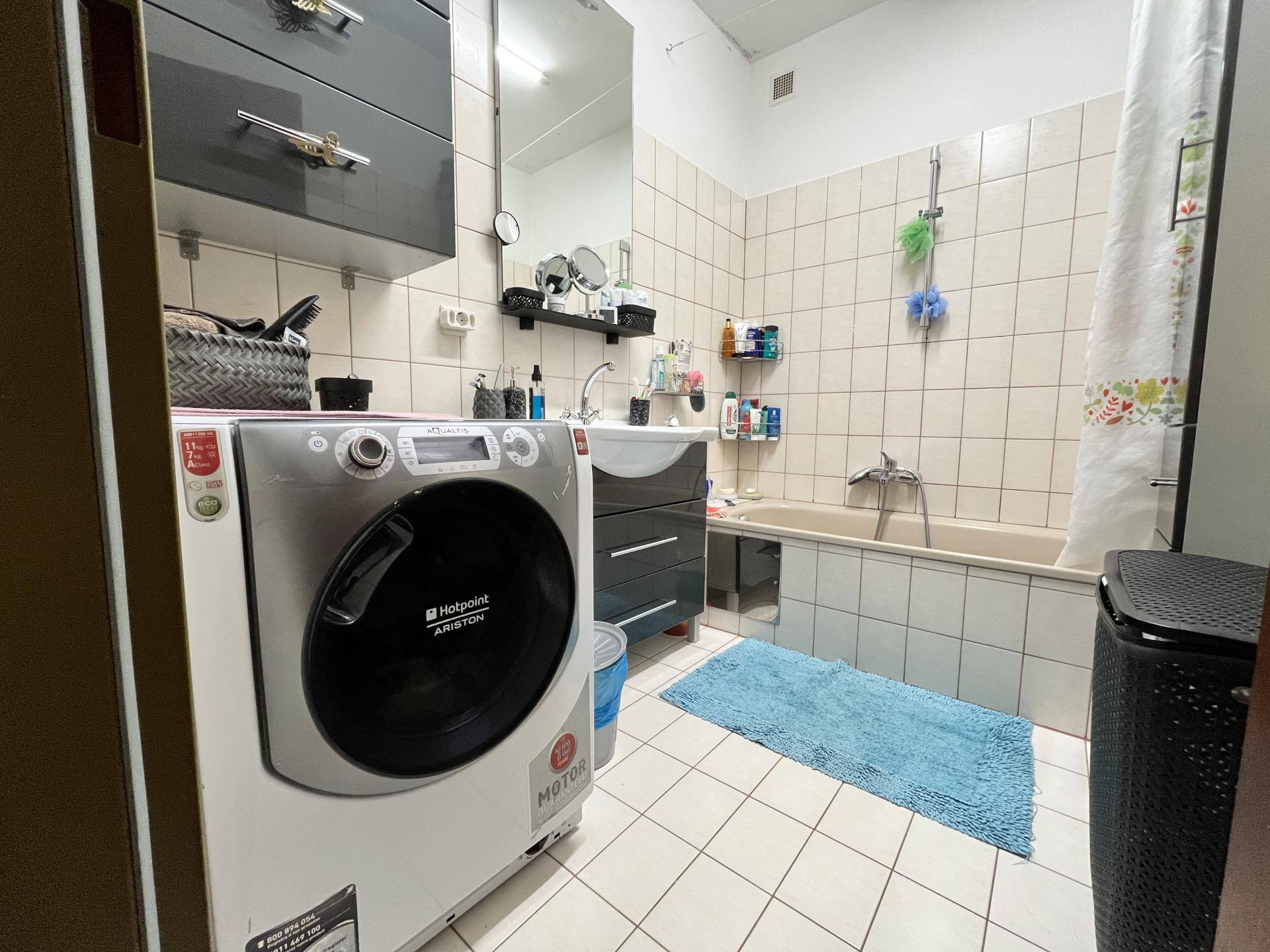 Badezimmer mit Badewanne, Waschbecken und integrierter Waschmaschine, hell gefliest.