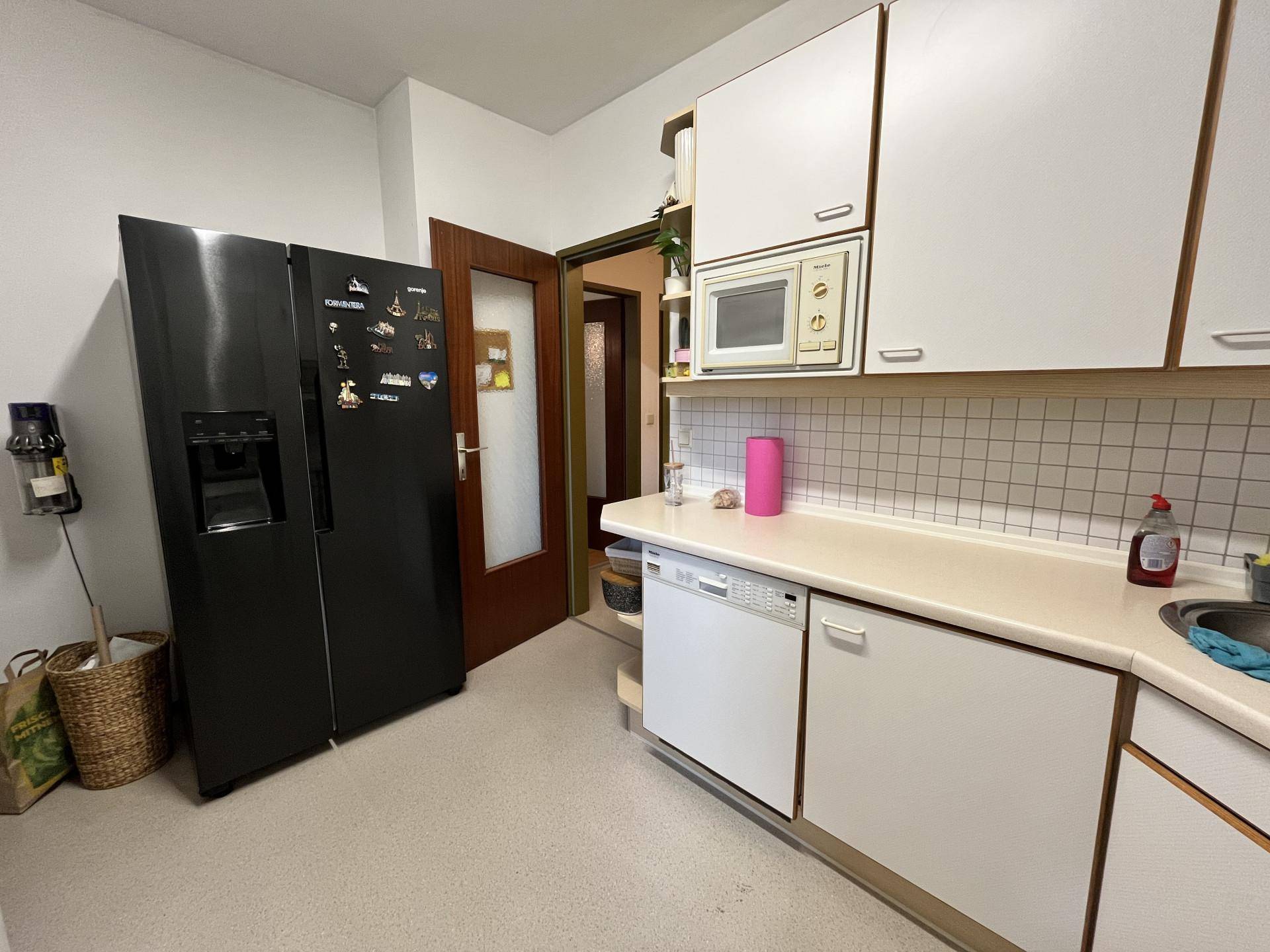 Küche mit großem schwarzem Kühlschrank, weißen Schränken und Durchgang zu einem anderen Raum.