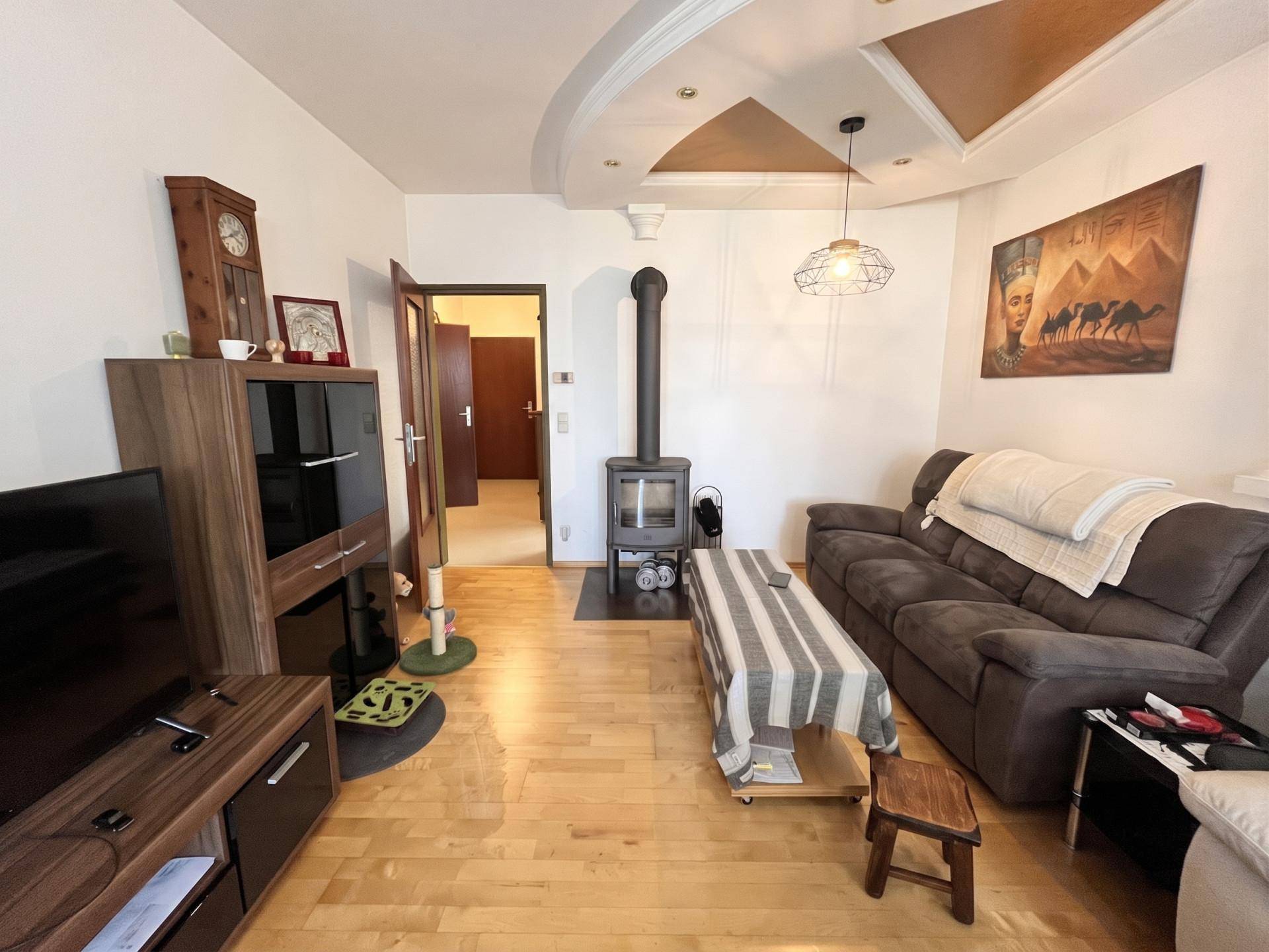 Geräumiges Wohnzimmer mit Sofa, Holzboden und einem gemütlichen Holzofen als Wärmequelle.