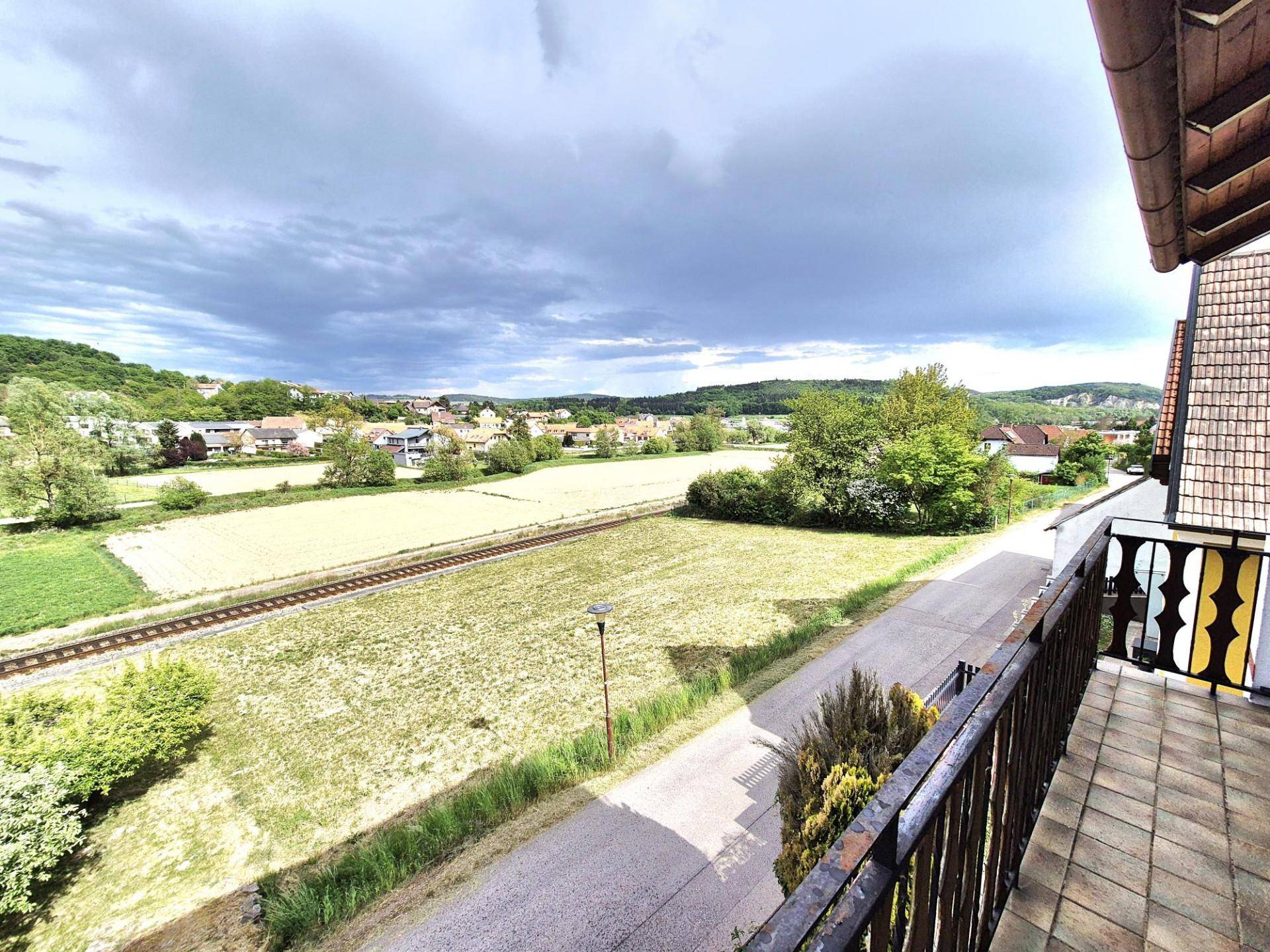 Weitläufiger Blick vom Balkon über Felder, eine Bahnlinie und die umliegende Landschaft mit Häusern.