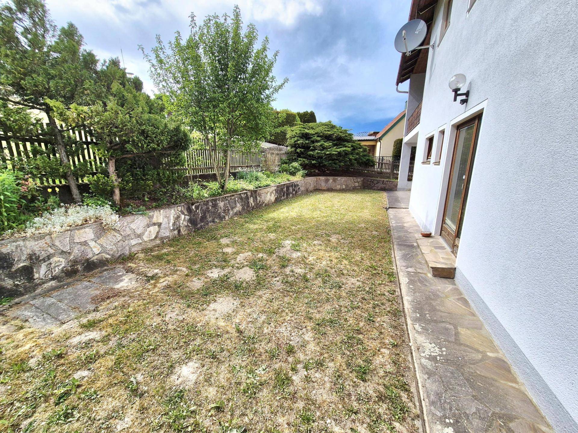Rasenfläche im Gartenbereich des Hauses, umgeben von einer Steinmauer und Bäumen im Hintergrund.