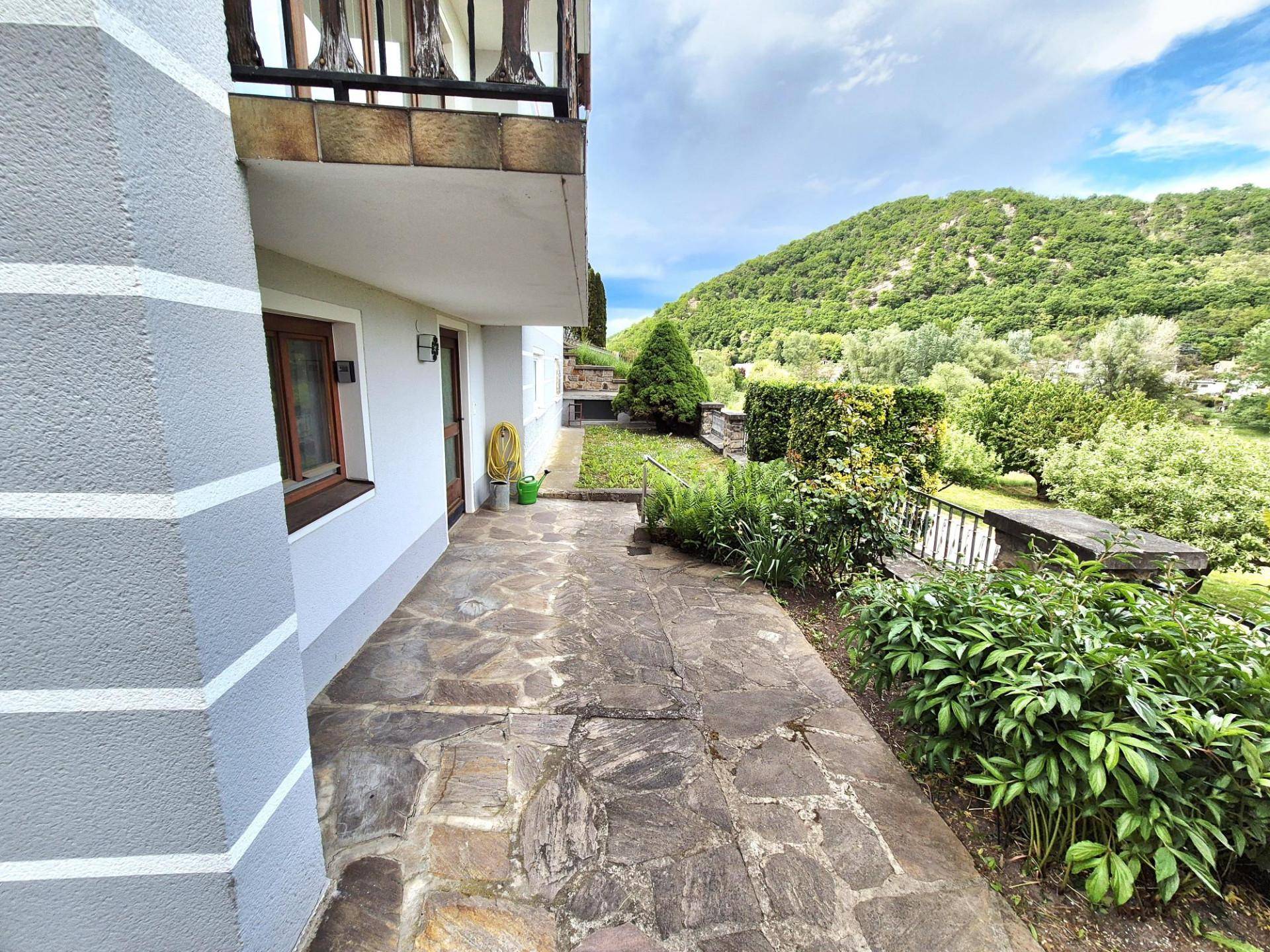 Gepflasterte Terrasse neben dem Haus mit Blick auf die umliegende grüne Hügellandschaft.