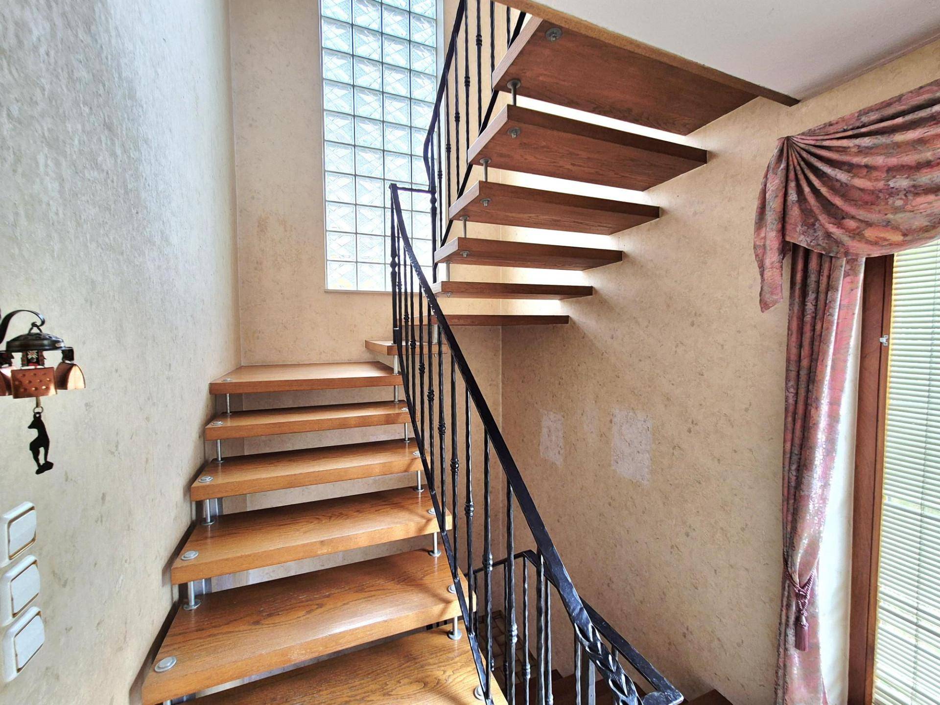 Holztreppe mit schmiedeeisernem Geländer und einem dekorativen Glasbausteinfenster.