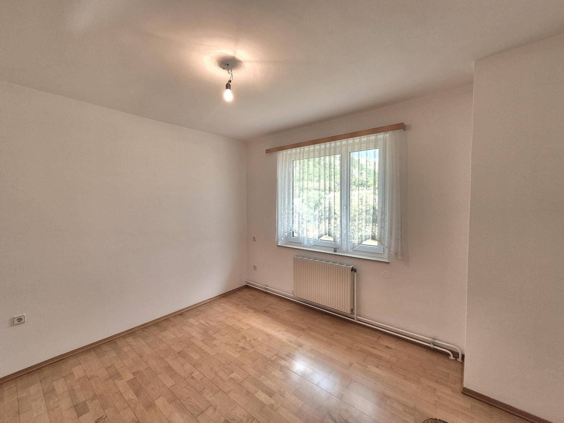 Helles Zimmer mit Parkettboden, weiß gestrichenen Wänden und einem Fenster mit Blick ins Grüne.
