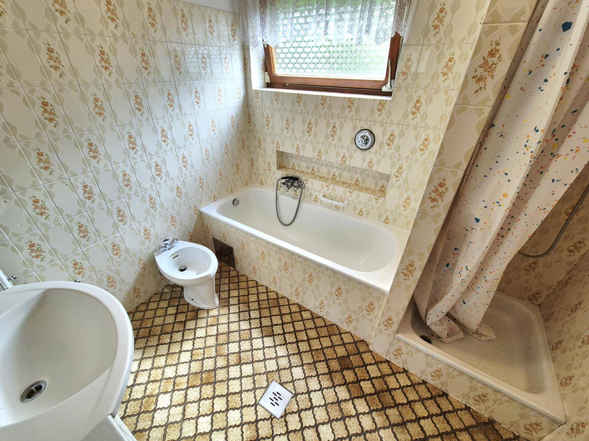 Badezimmer mit gemusterten Fliesen, Badewanne, Dusche und Bidet, sowie einem Fenster.