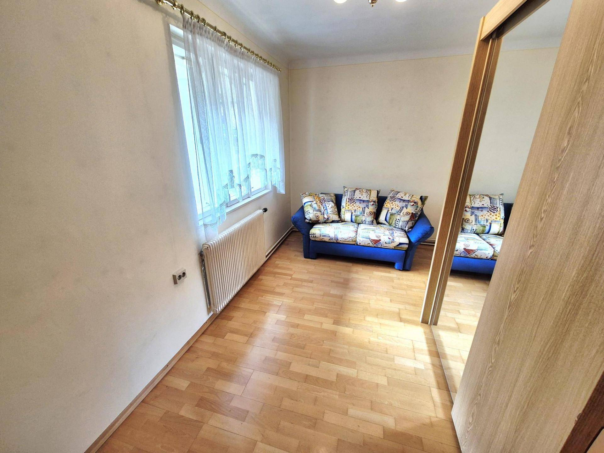 Kleines Zimmer mit Holzboden, einem blauen Sofa und einem Fenster mit Vorhängen.
