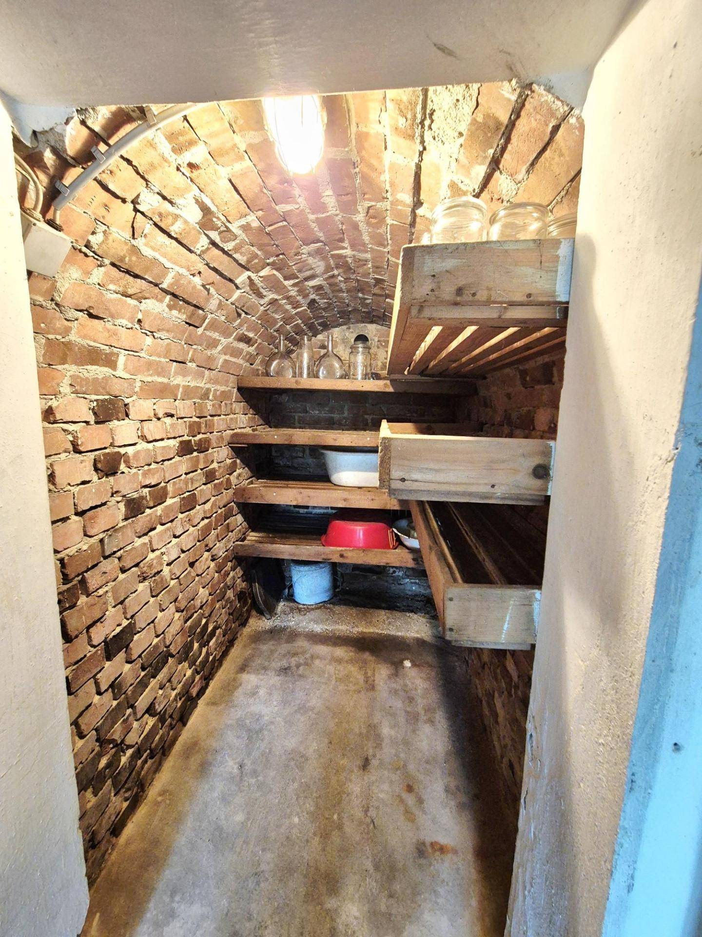 Historischer Gewölbekeller mit unverputzten Ziegelwänden und einfachen Holzregalen für Lagerzwecke.