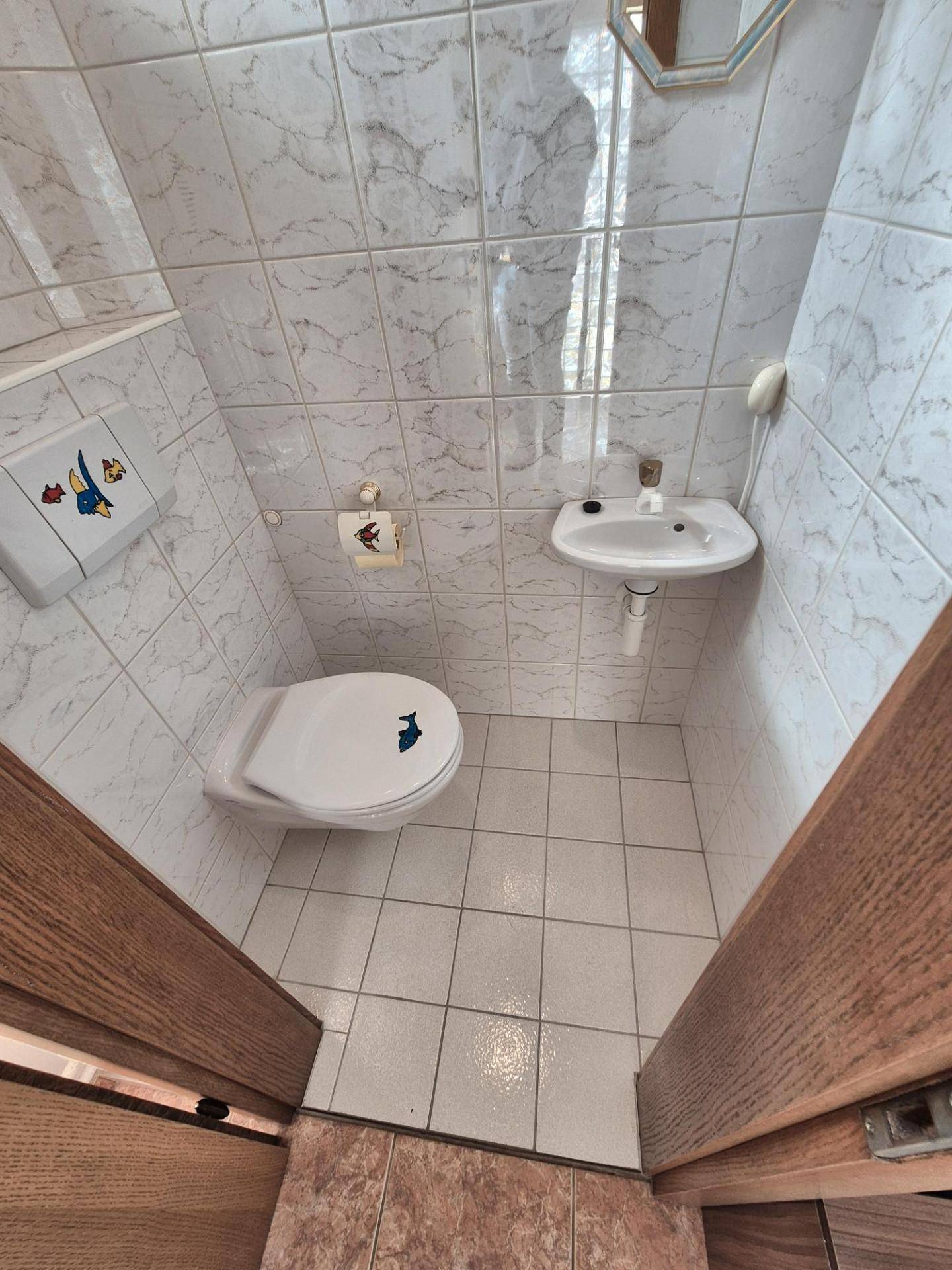 Kleines Gäste-WC mit weißen Fliesen, Toilette und einem Waschbecken.