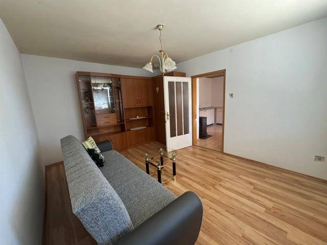 Wohnzimmer mit Laminatboden, einem Sofa und einem Holzschrank, der zu einem weiteren Raum führt.