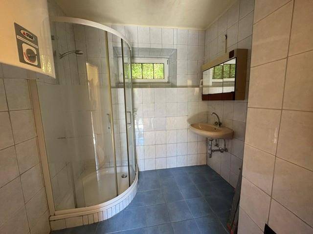 Badezimmer mit Duschkabine, Waschbecken und hellblauen Fliesen, inklusive Fenster für Tageslicht.