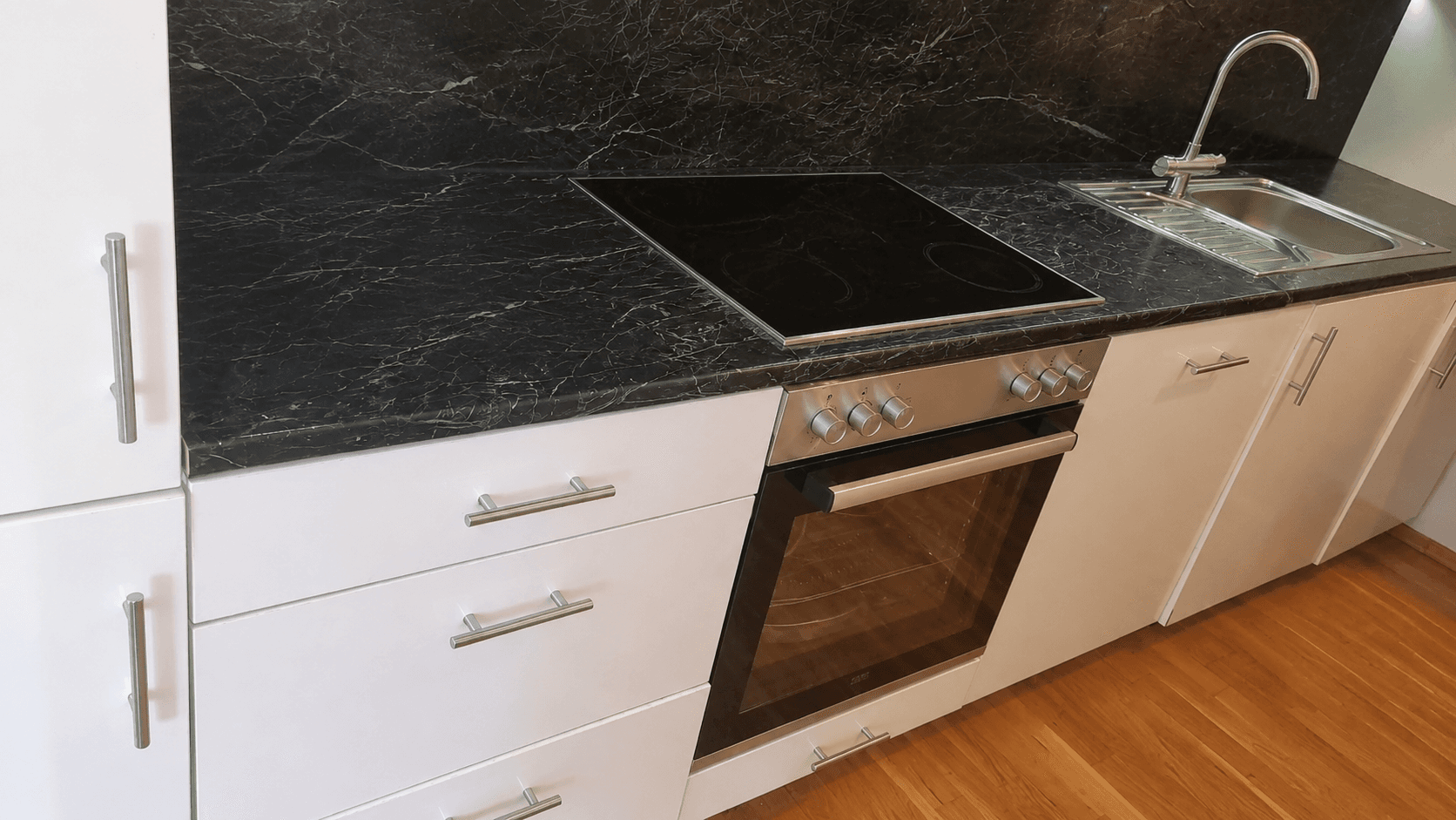 Moderne Küche mit schwarzen Marmor-Arbeitsplatten, Induktionskochfeld und integriertem Backofen.
