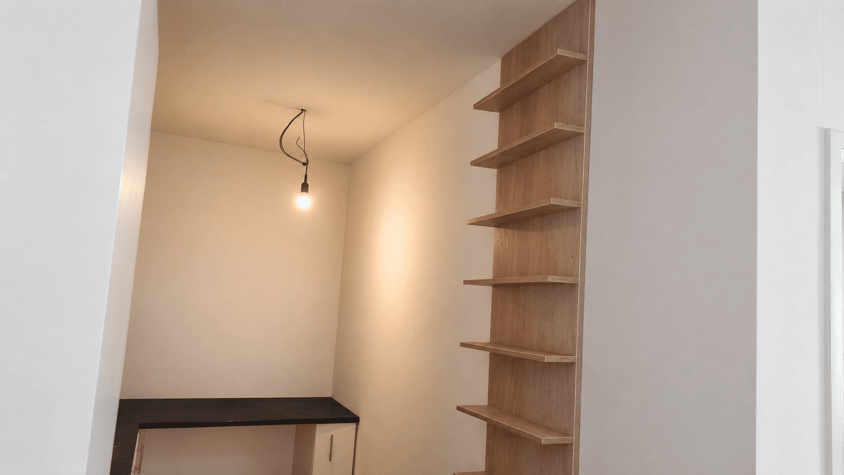 Kleiner Raum mit Holzregalen, einem Schreibtisch und einfacher Beleuchtung, ideal als Arbeitsbereich.