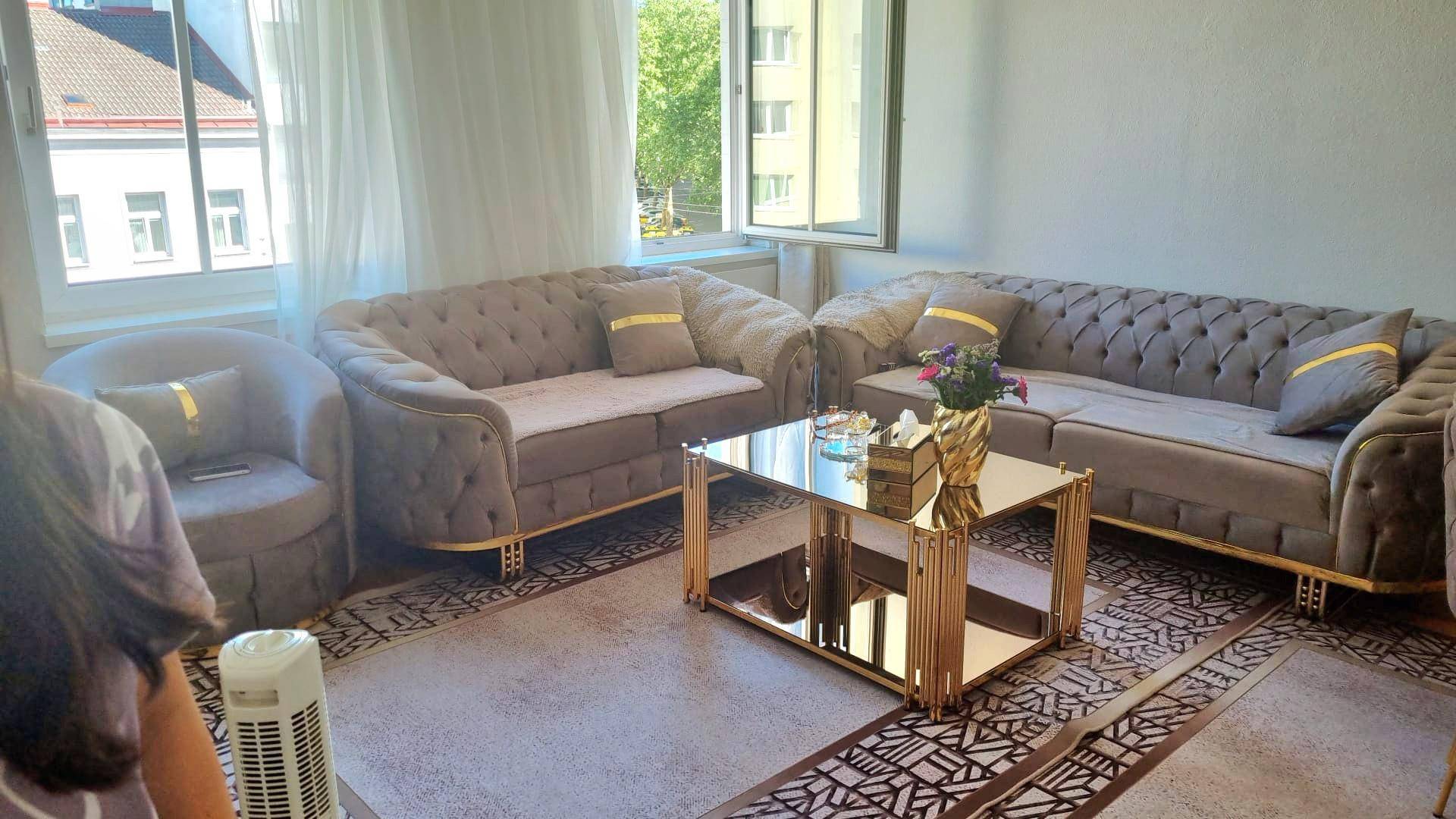 Helles Wohnzimmer mit eleganten grauen Sofas, einem glänzenden Couchtisch und großen Fenstern.